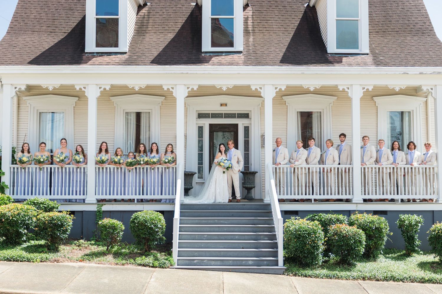 Wedding party posing on the wraparound porch of a elegant white Southern plantation venue.