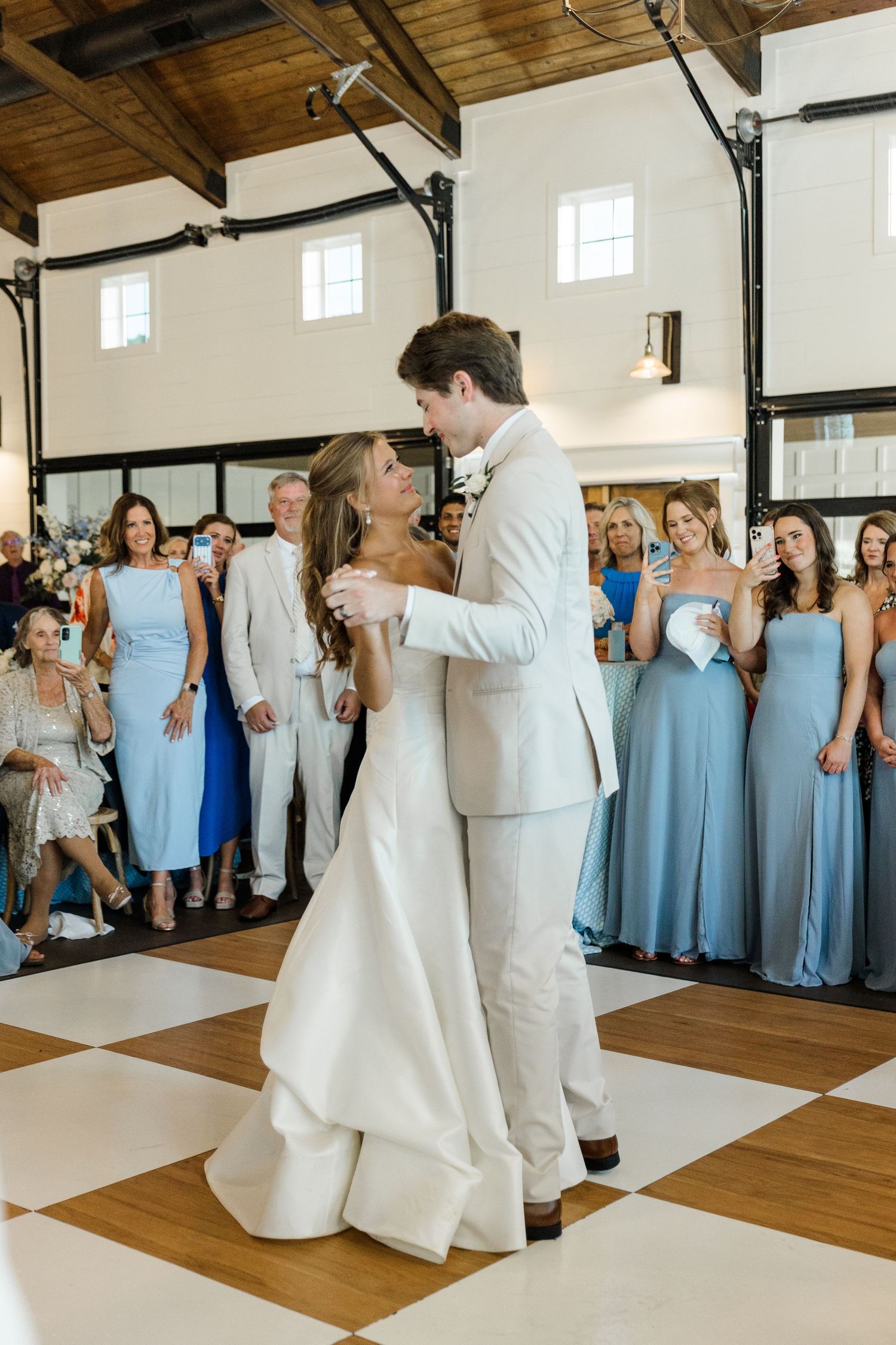 Bride and groom share their first dance on a checkered floor, surrounded by bridesmaids in blue at their wedding reception.