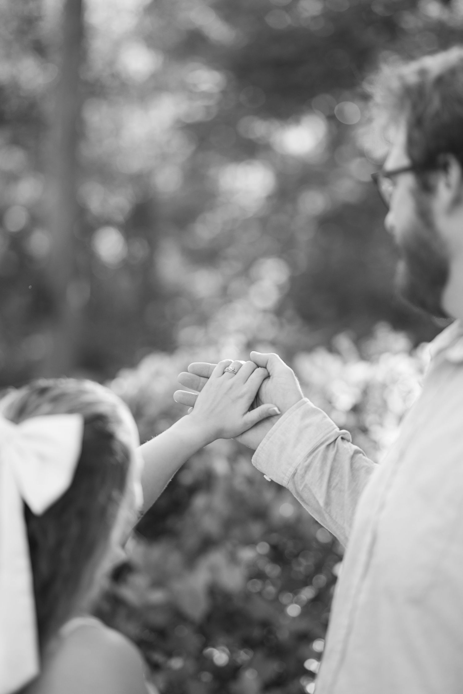 Black and white photo of a child holding a father's hand outdoors among trees.