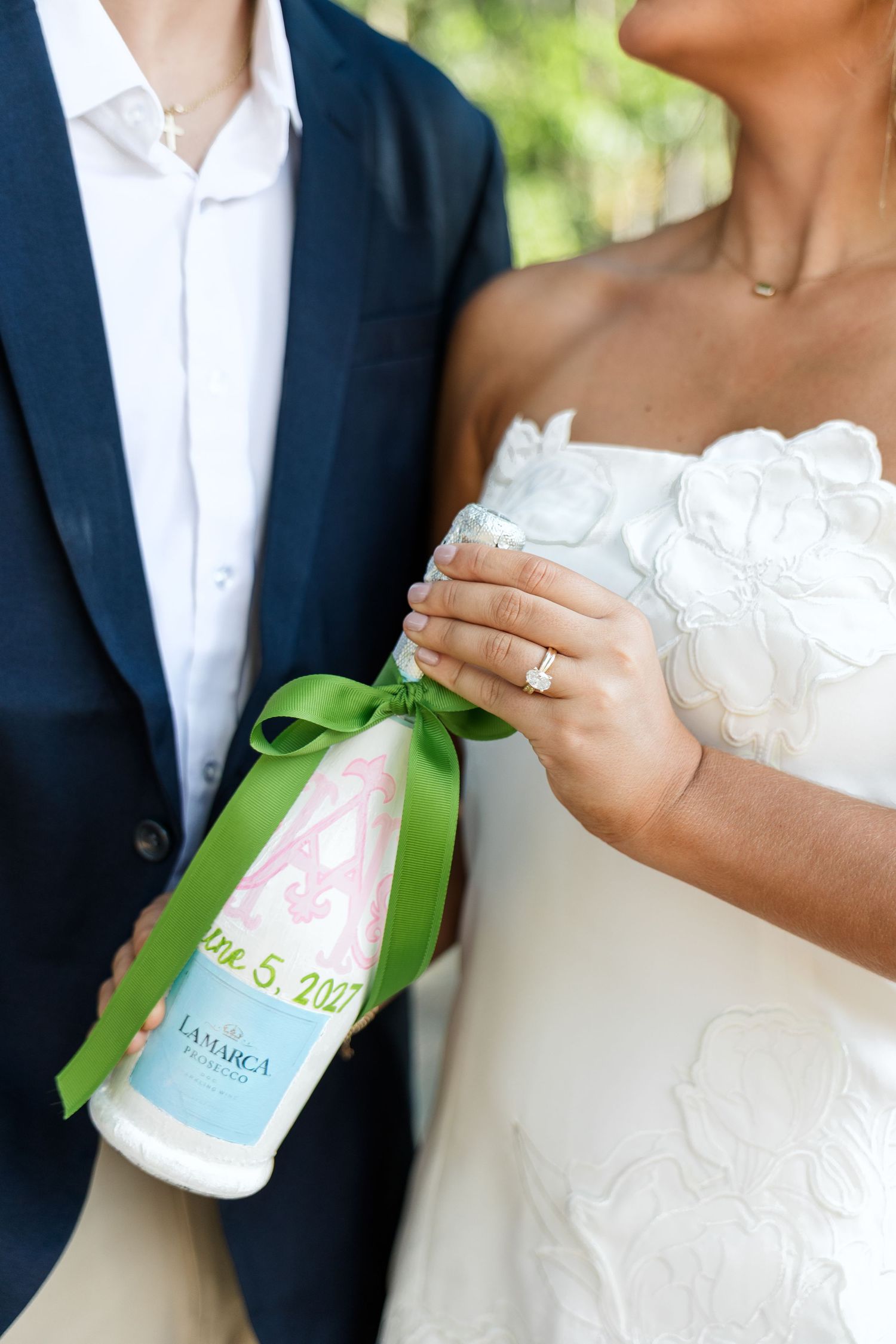 Bride and groom holding a custom La Marca champagne bottle with green ribbon and monogram label dated June 5, 2021.
