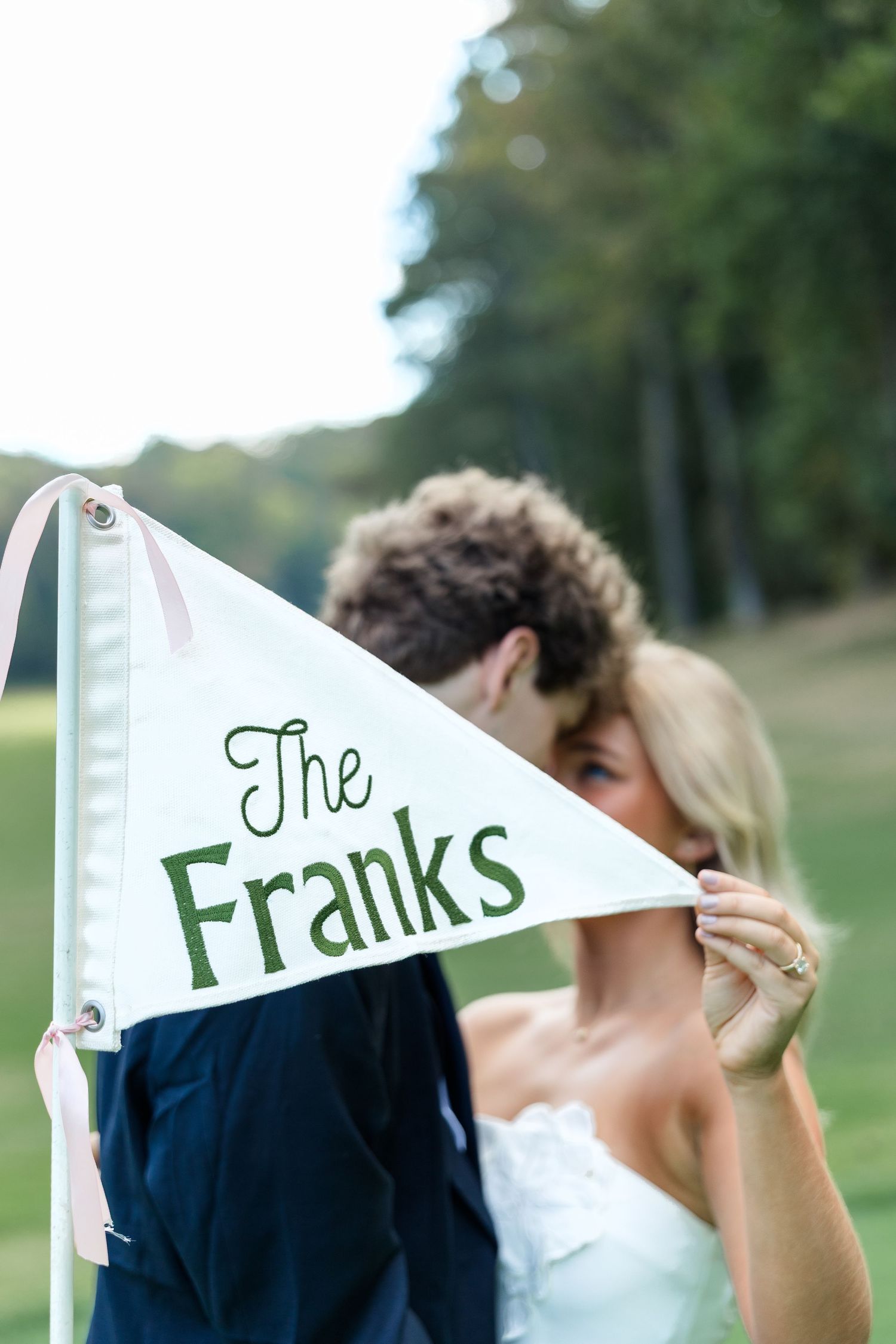 Newlyweds kissing behind a white pennant flag reading The Franks at an outdoor wedding ceremony.