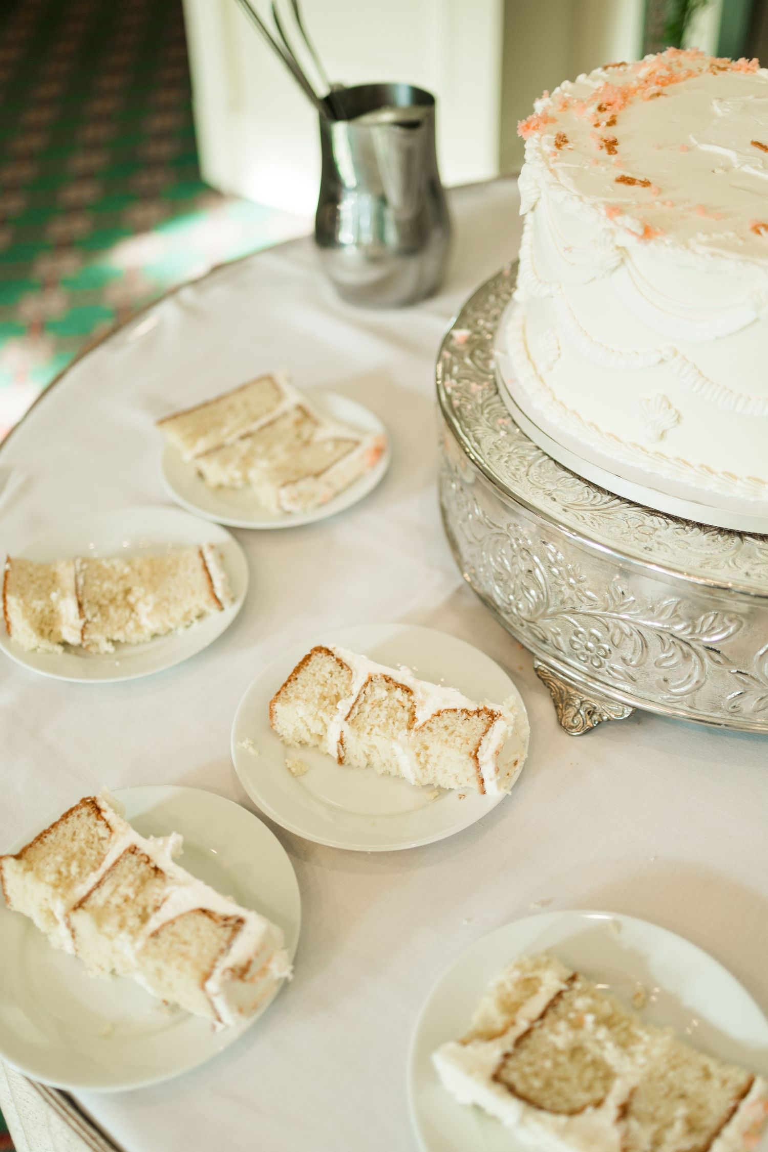 Sliced white wedding cake pieces plated on white dishes beside a tiered cake on a silver stand.
