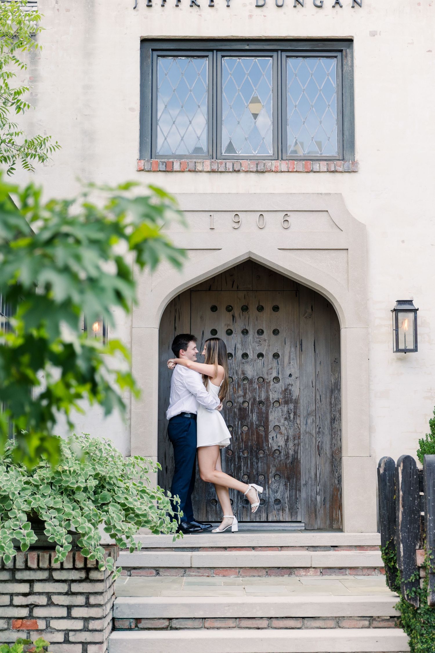Couple embracing in arched doorway of historic 1906 Jeffrey Dungan building with ornate wooden door.