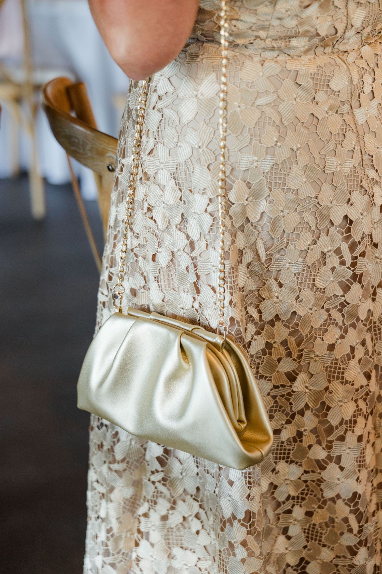 Close-up of gold satin clutch purse worn by guest in cream lace dress at wedding reception.