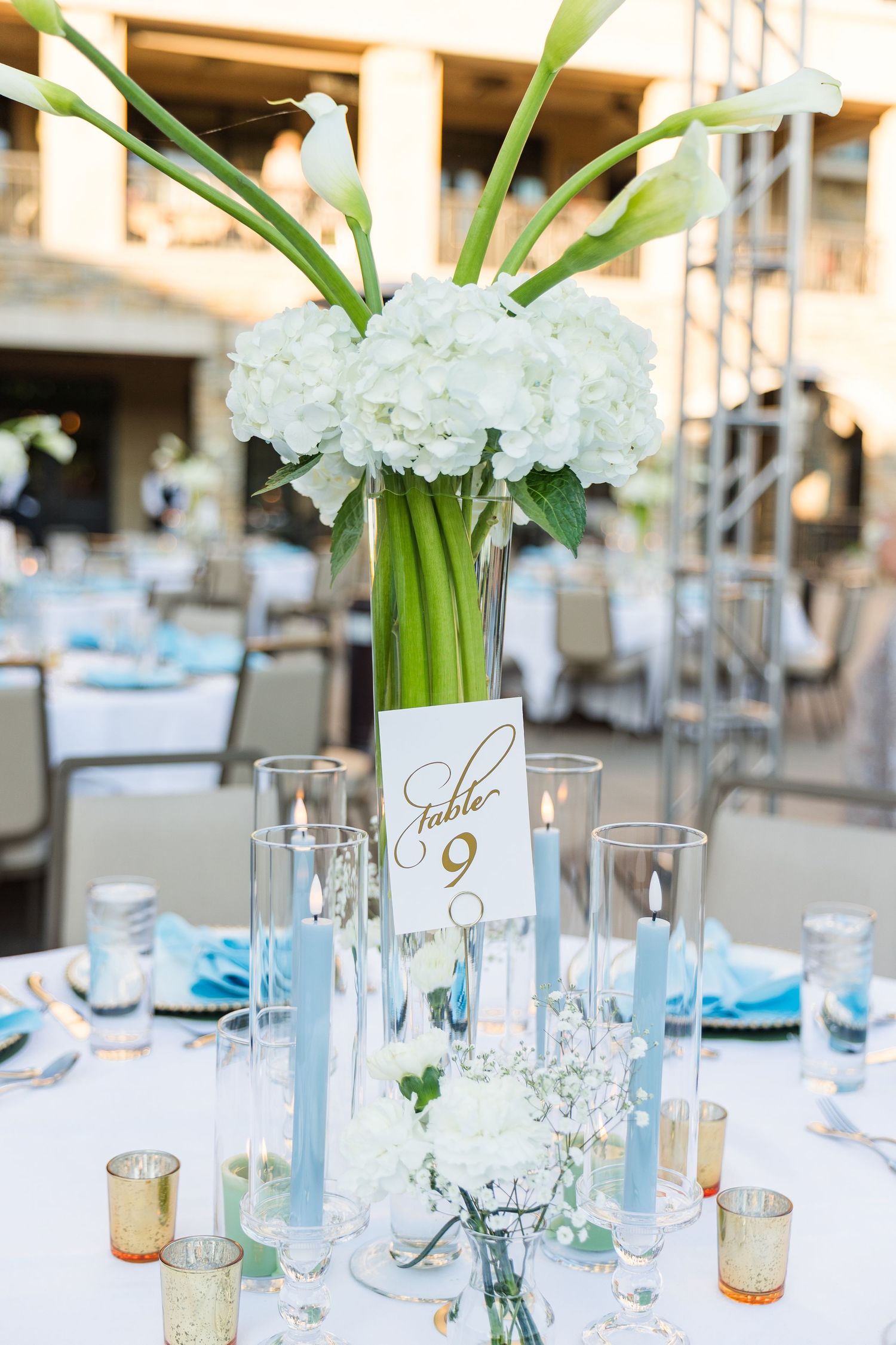 Elegant wedding table centerpiece with white hydrangeas, calla lilies, blue taper candles, and a Table 9 card.