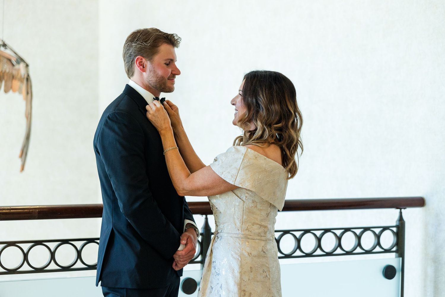 Bride adjusting groom's bow tie before wedding ceremony, sharing a tender moment in elegant venue.