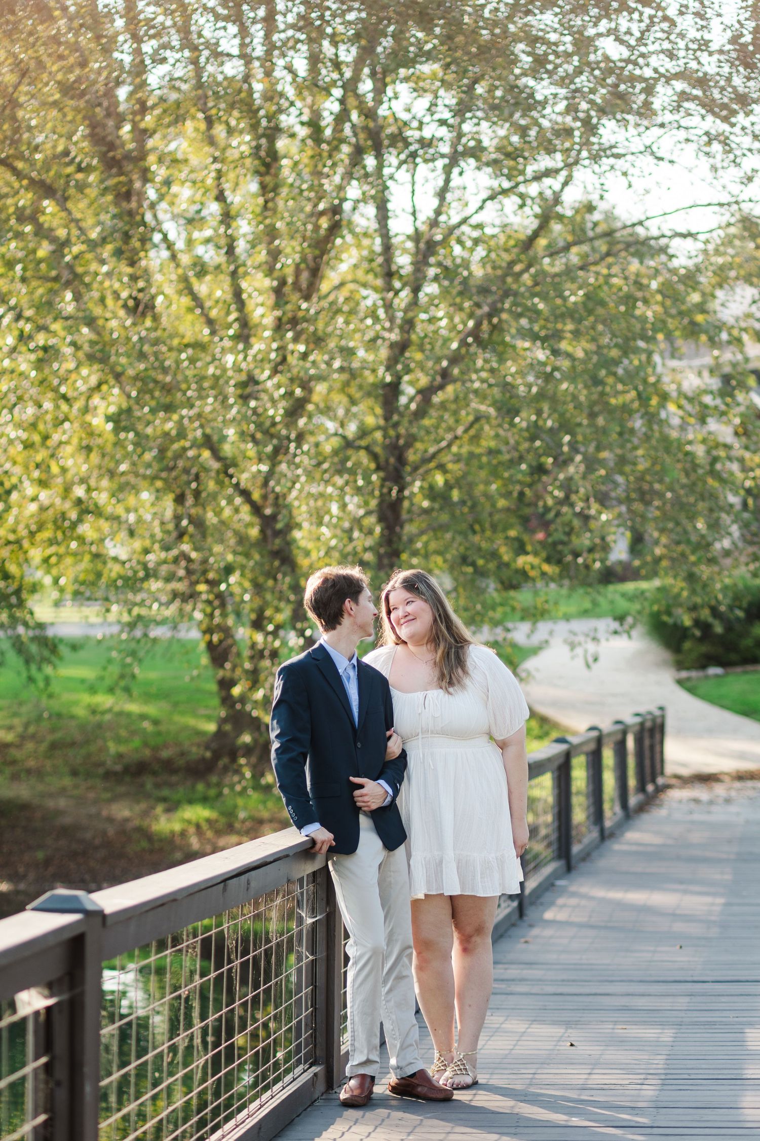 Couple in love posing on a wooden bridge surrounded by lush green trees during a sunny outdoor engagement session.