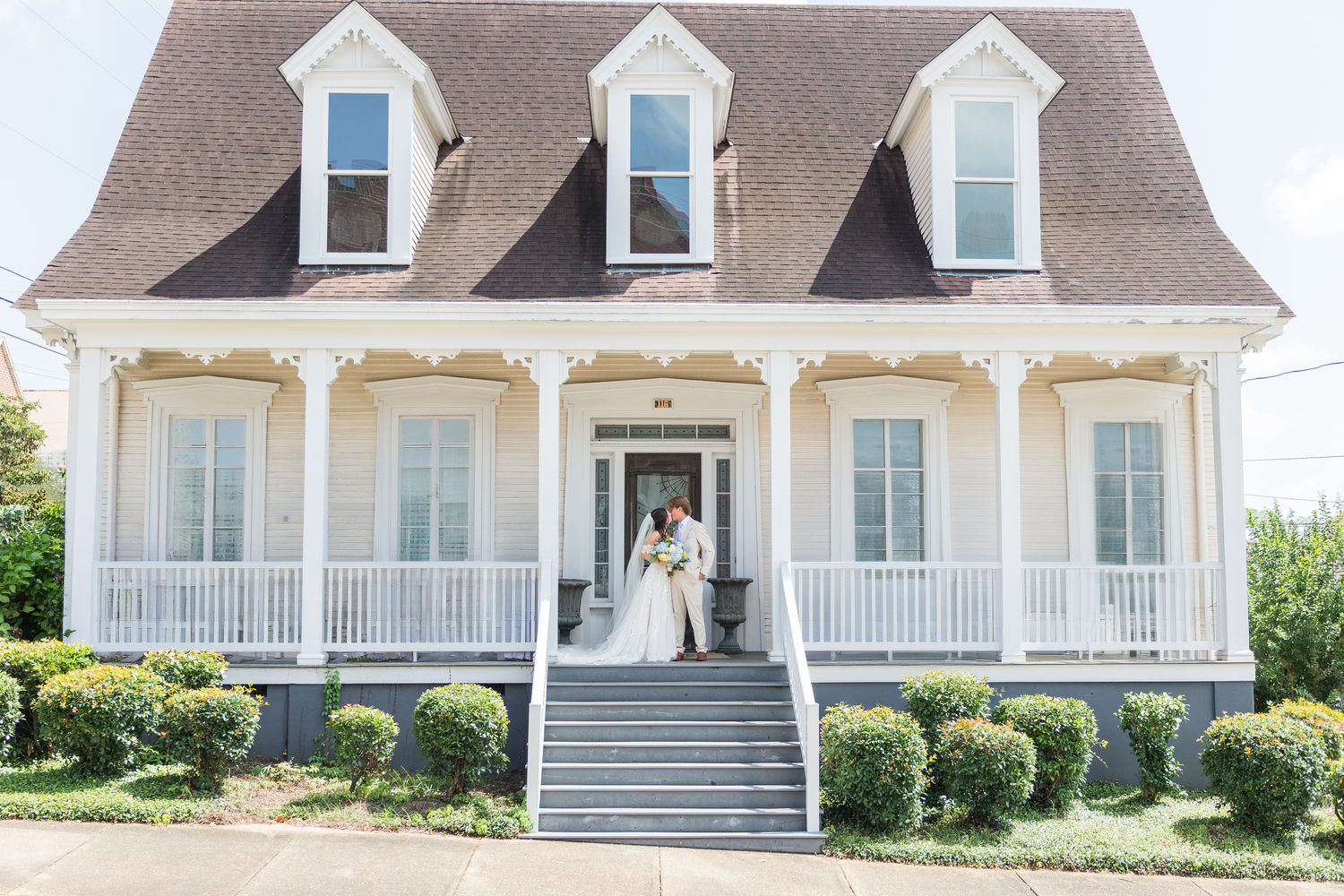 Bride and groom embrace on the porch of a charming white Southern-style wedding venue.