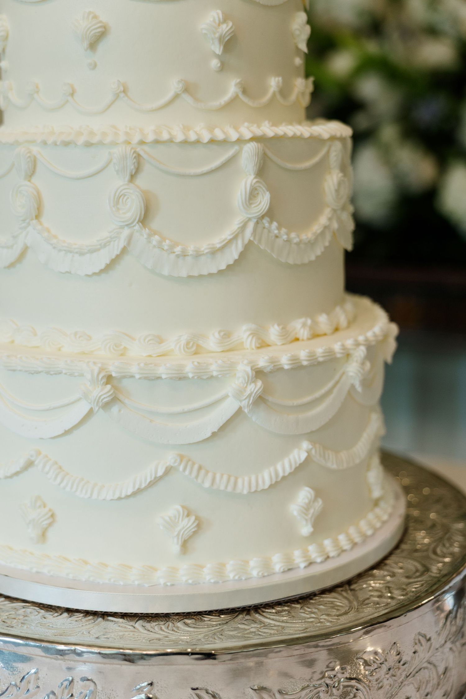 Elegant three-tier white wedding cake with intricate fondant swag details on a silver cake stand.