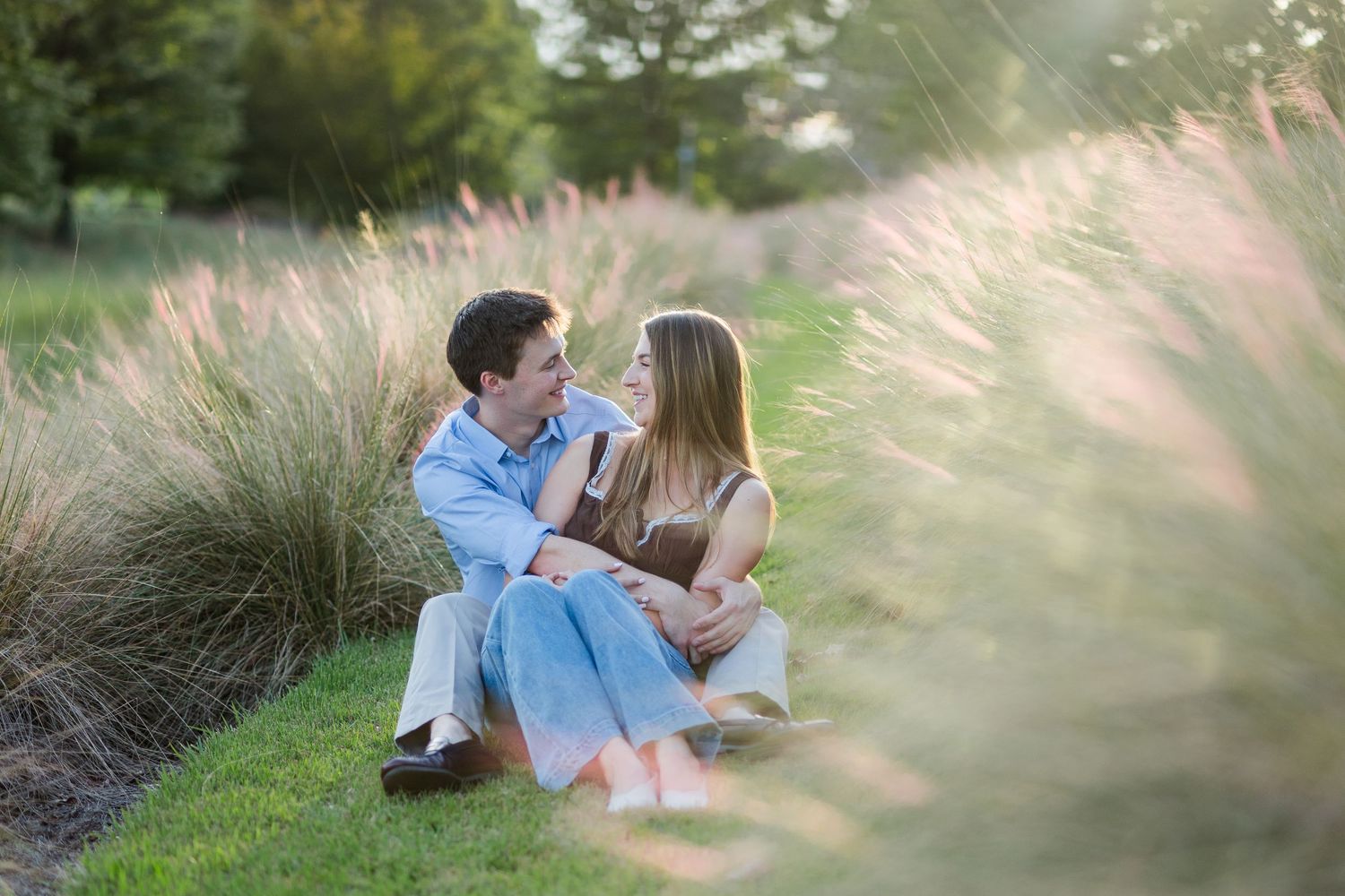 Romantic couple sitting together on grass surrounded by tall ornamental pampas grass in a park.