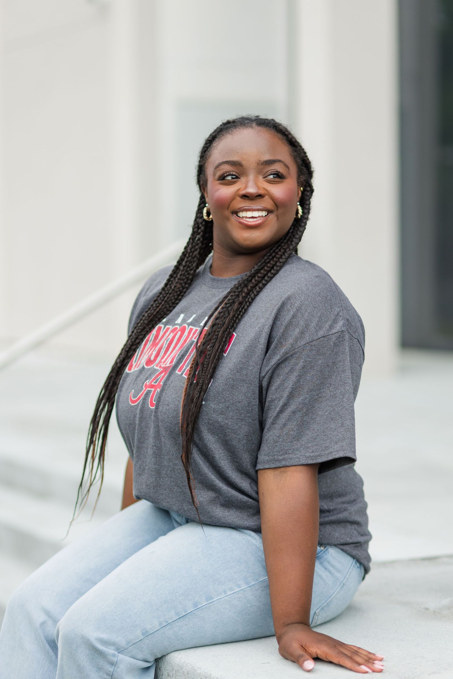 Smiling young woman in Alabama Crimson Tide gray t-shirt and jeans sitting outdoors on steps.