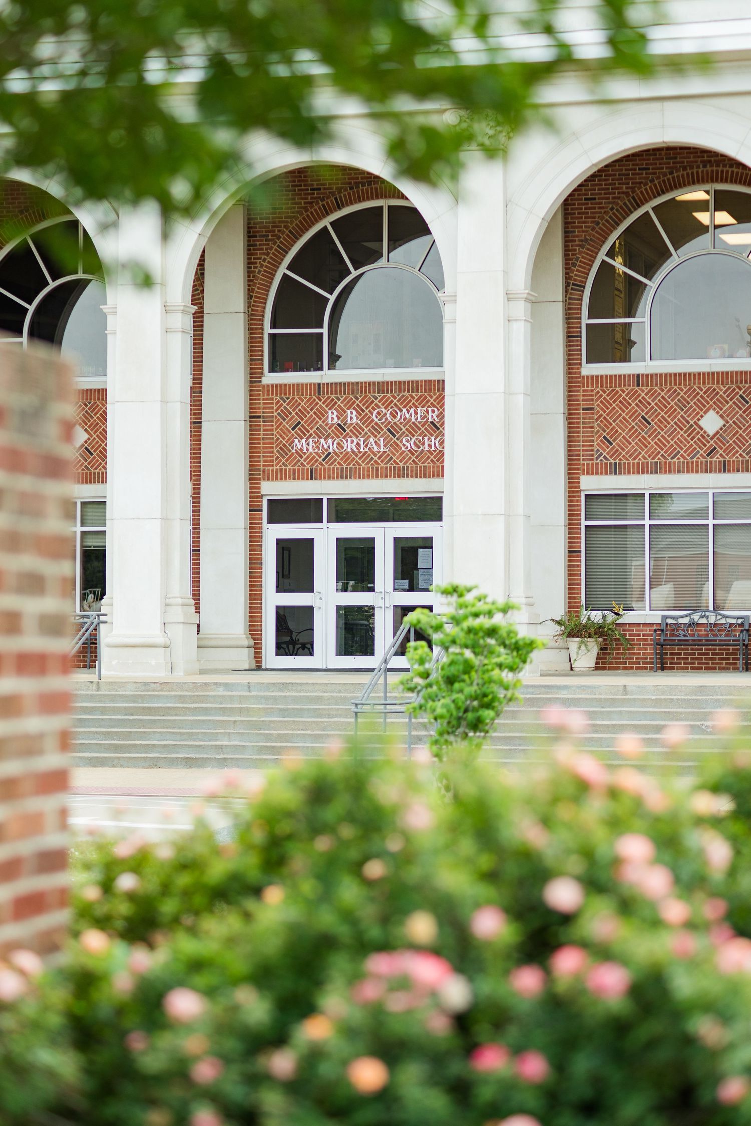 Exterior view of B.B. Comer Memorial School brick building with arched windows and lush greenery.