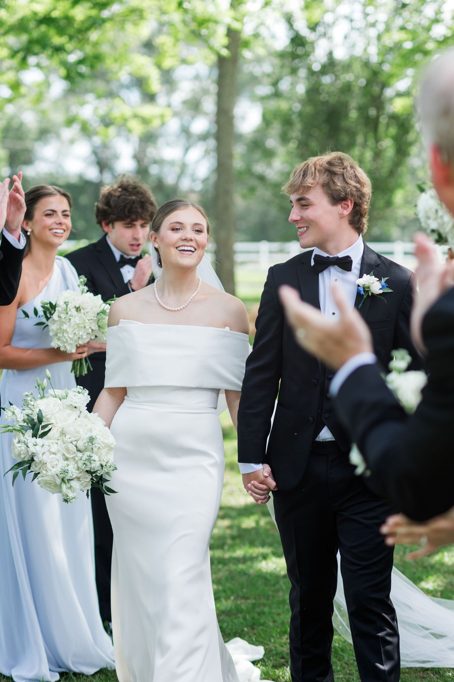 Bride and groom walking hand in hand after their outdoor wedding ceremony with bridal party.