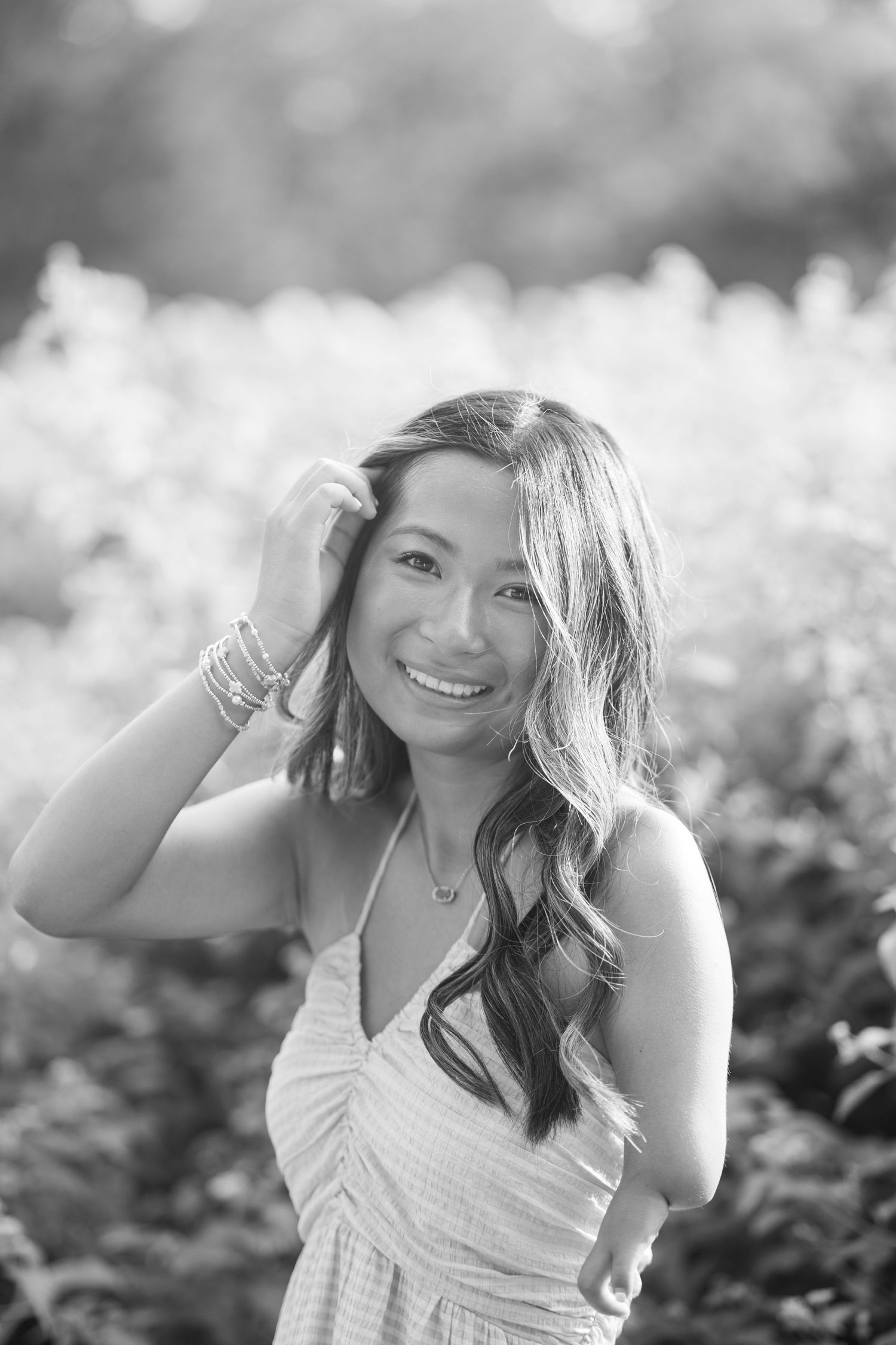 Black and white portrait of smiling young woman with wavy hair in sunny field.