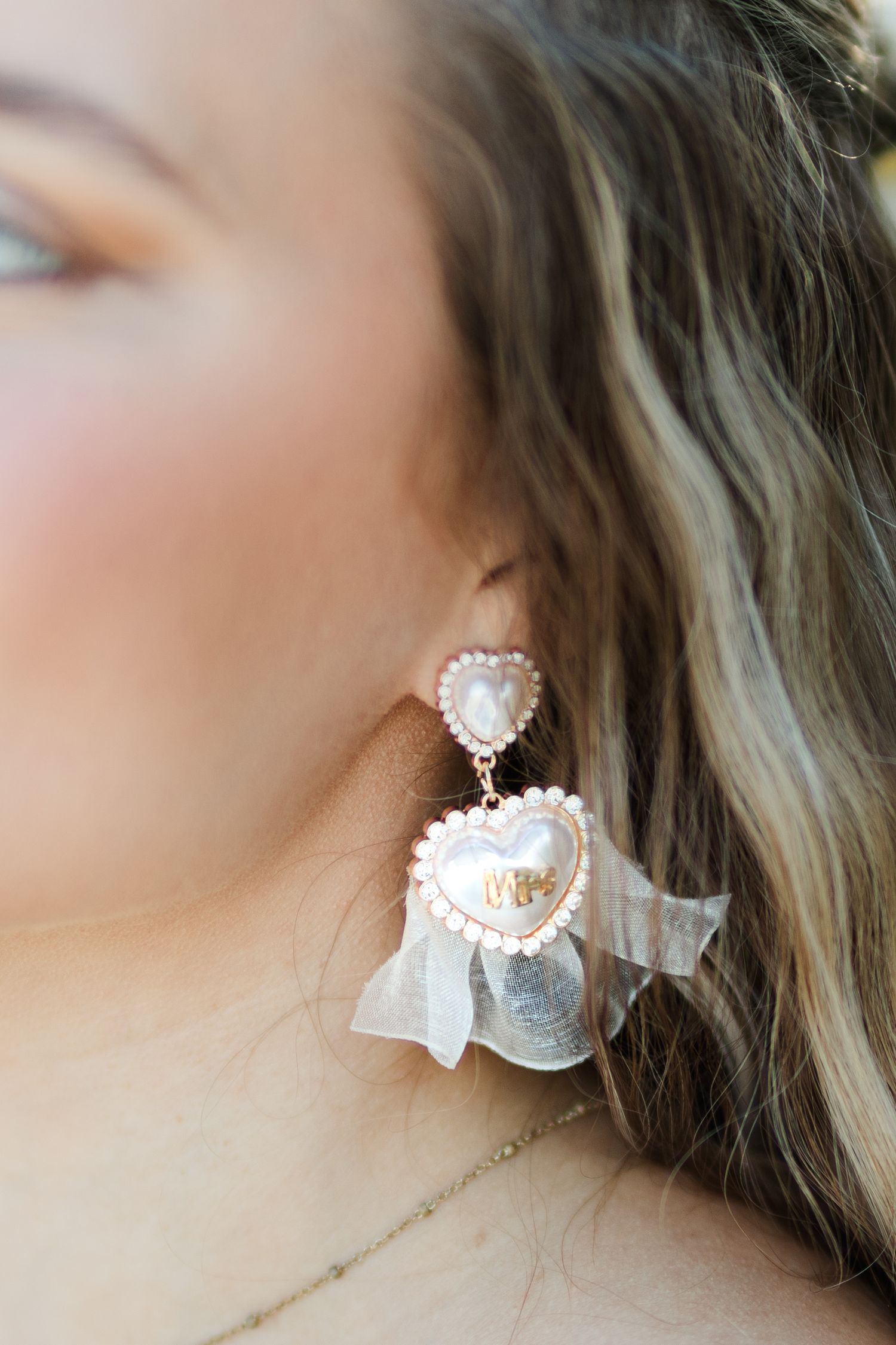 Close-up of a woman wearing elegant rose gold heart-shaped earrings with pearls and sheer bow detail.