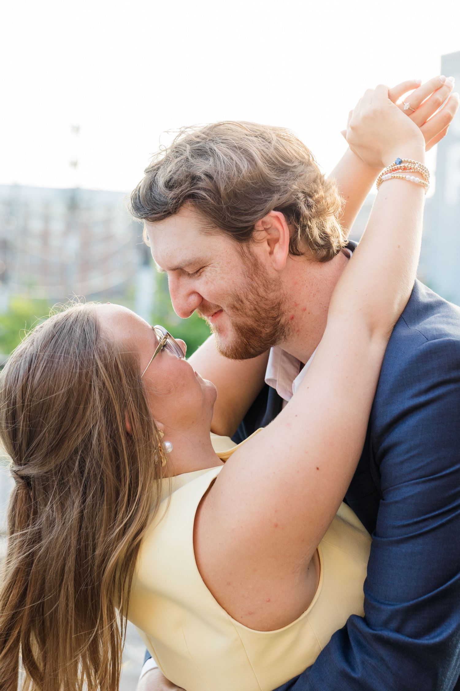 A joyful couple shares a romantic moment outdoors, with the woman in yellow embracing the bearded man in a navy suit.