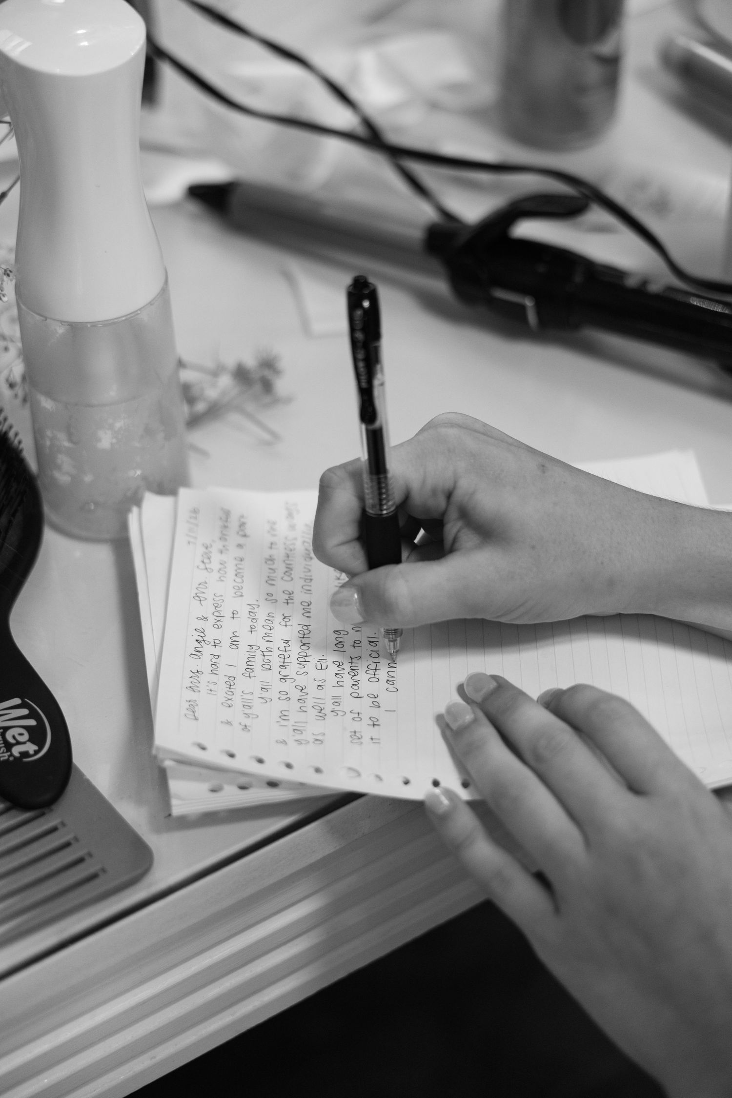 Black and white photo of bride writing personal vows in notepad at vanity table before wedding ceremony.