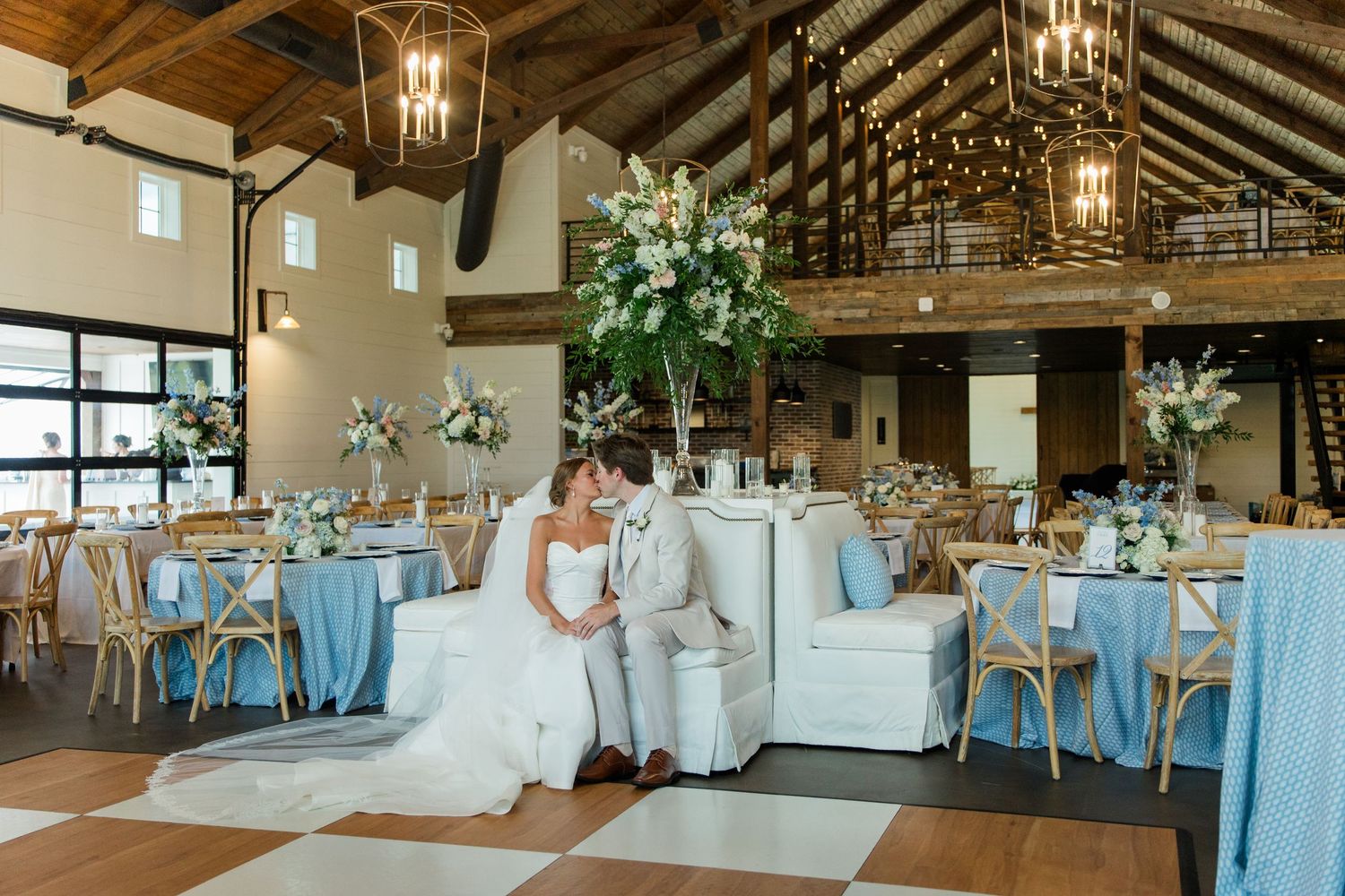 Bride and groom share a romantic moment in an elegant barn wedding venue with blue table linens and floral centerpieces.