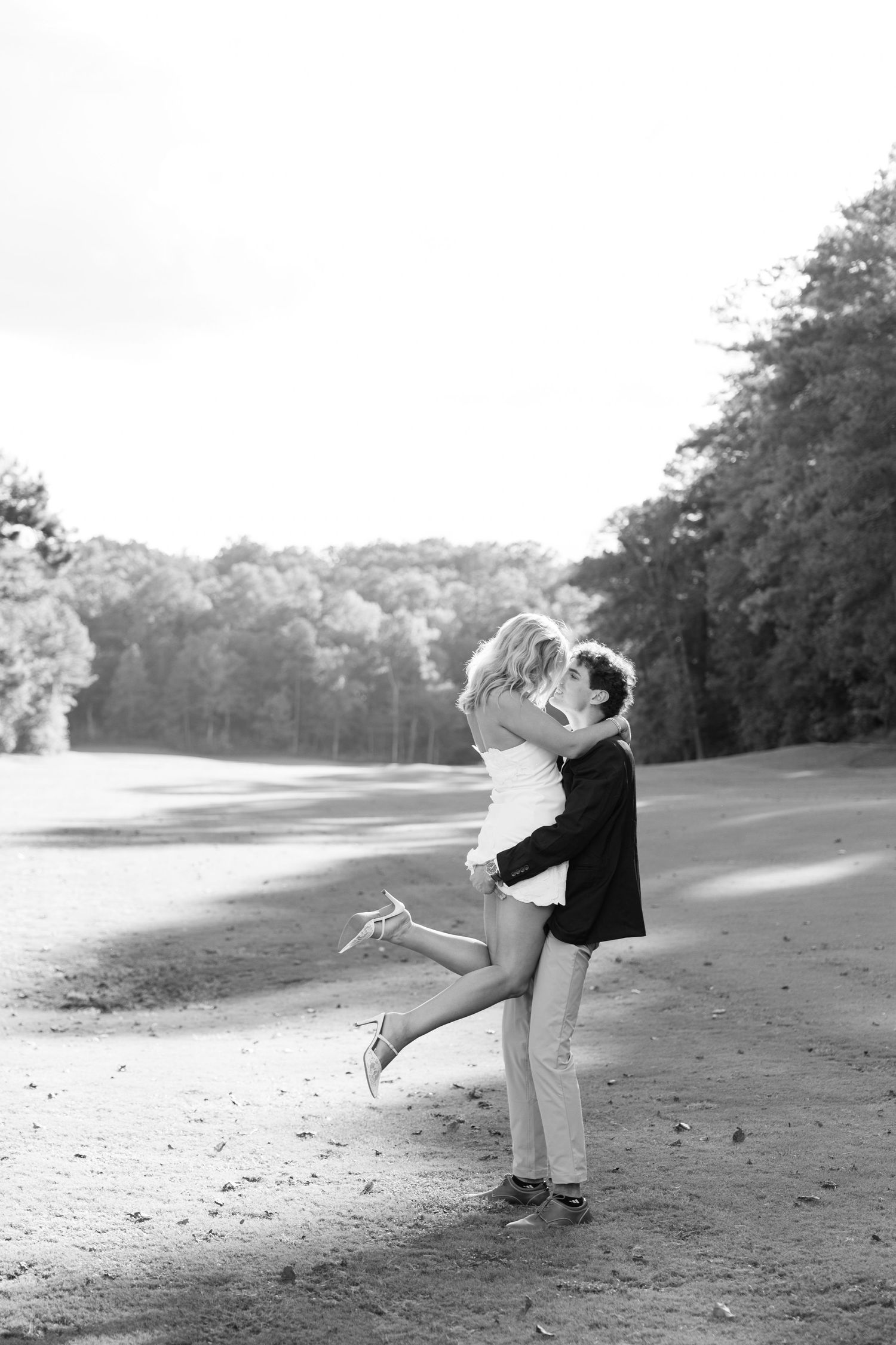 Black and white photo of couple embracing and kissing on golf course path.