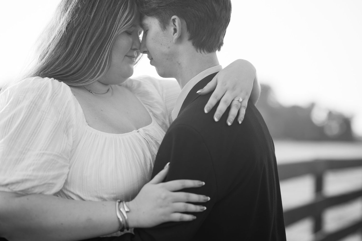 Black and white photo of a couple sharing a romantic moment, woman in white dress embracing man in dark suit outdoors.
