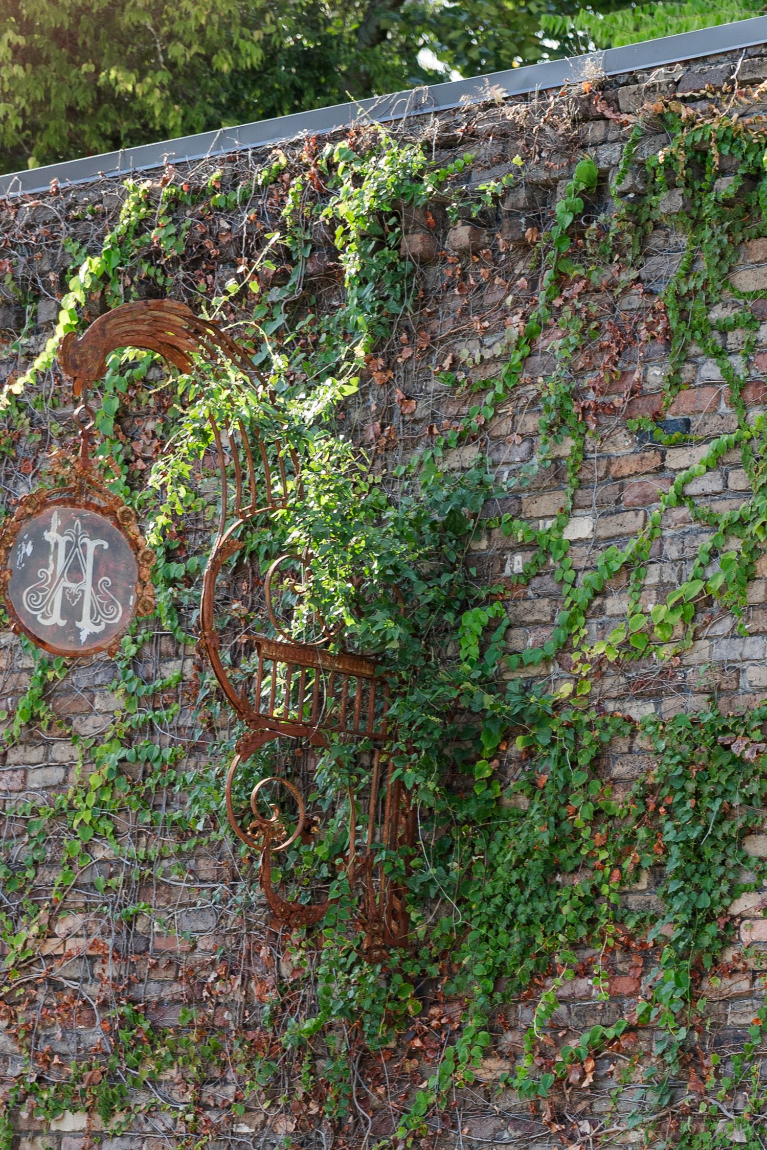 Rustic ivy-covered brick wall with ornate vintage metal monogram letter H decorative garden gate.