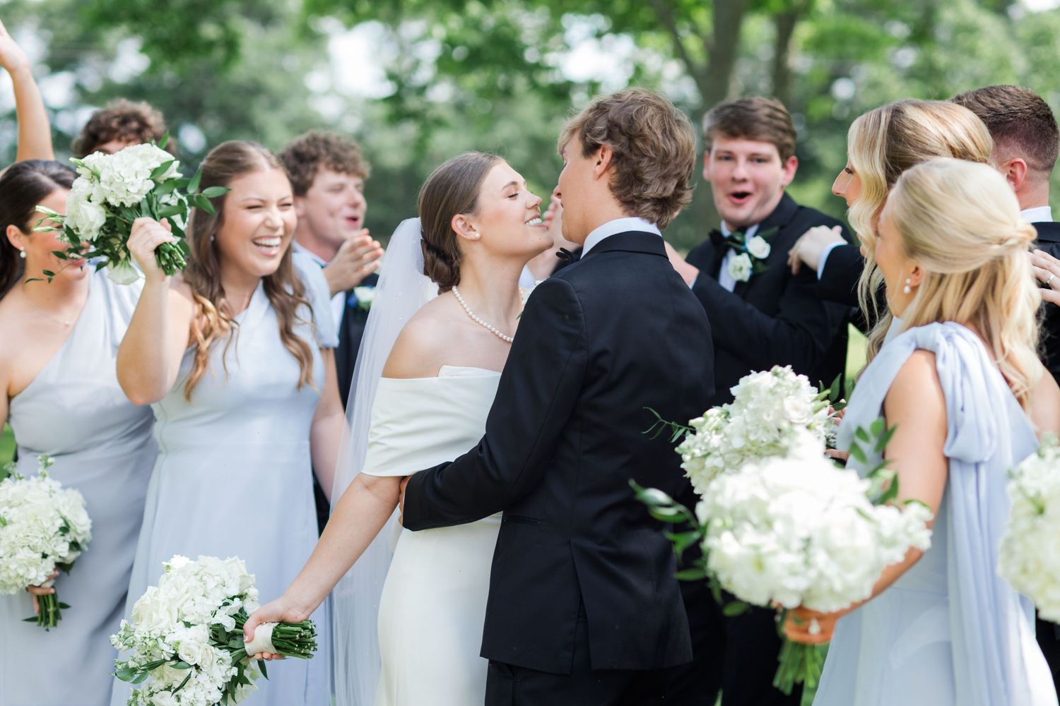 Bride and groom sharing a kiss surrounded by bridesmaids in light blue dresses at wedding.