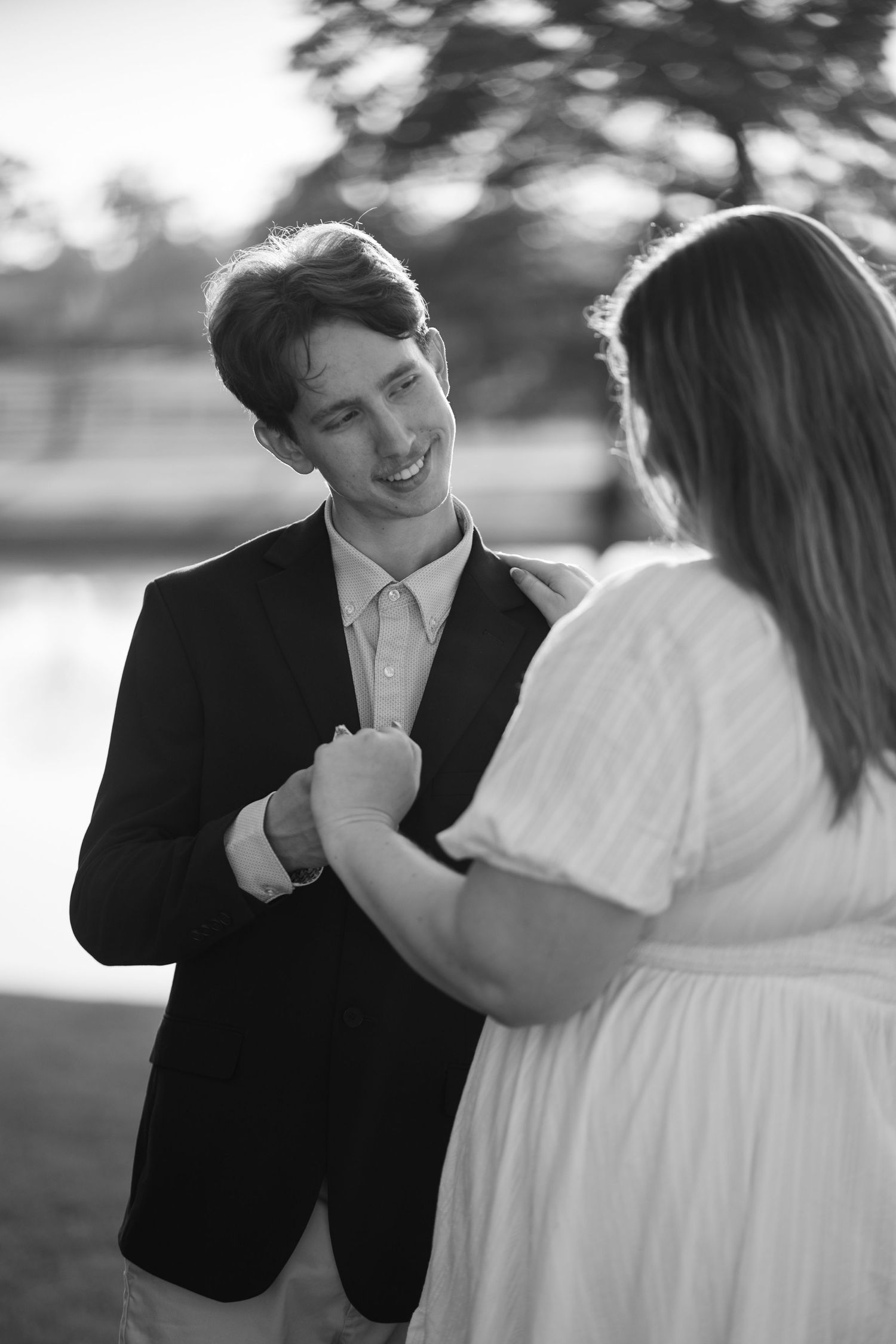 Black and white photo of smiling groom holding hands with bride during romantic outdoor session.