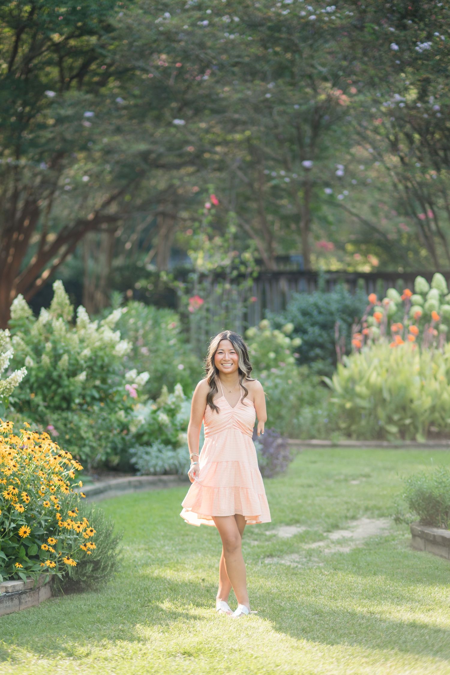 Young woman in a peach dress walking through a lush garden with colorful flowers on a sunny day.