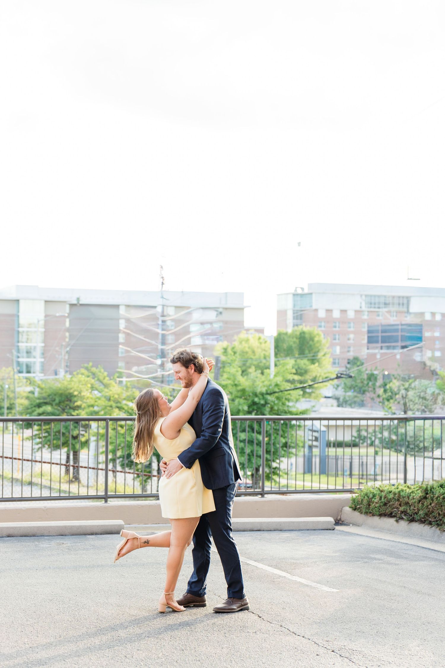 Couple embracing and kissing on rooftop parking lot during outdoor urban engagement photo session.