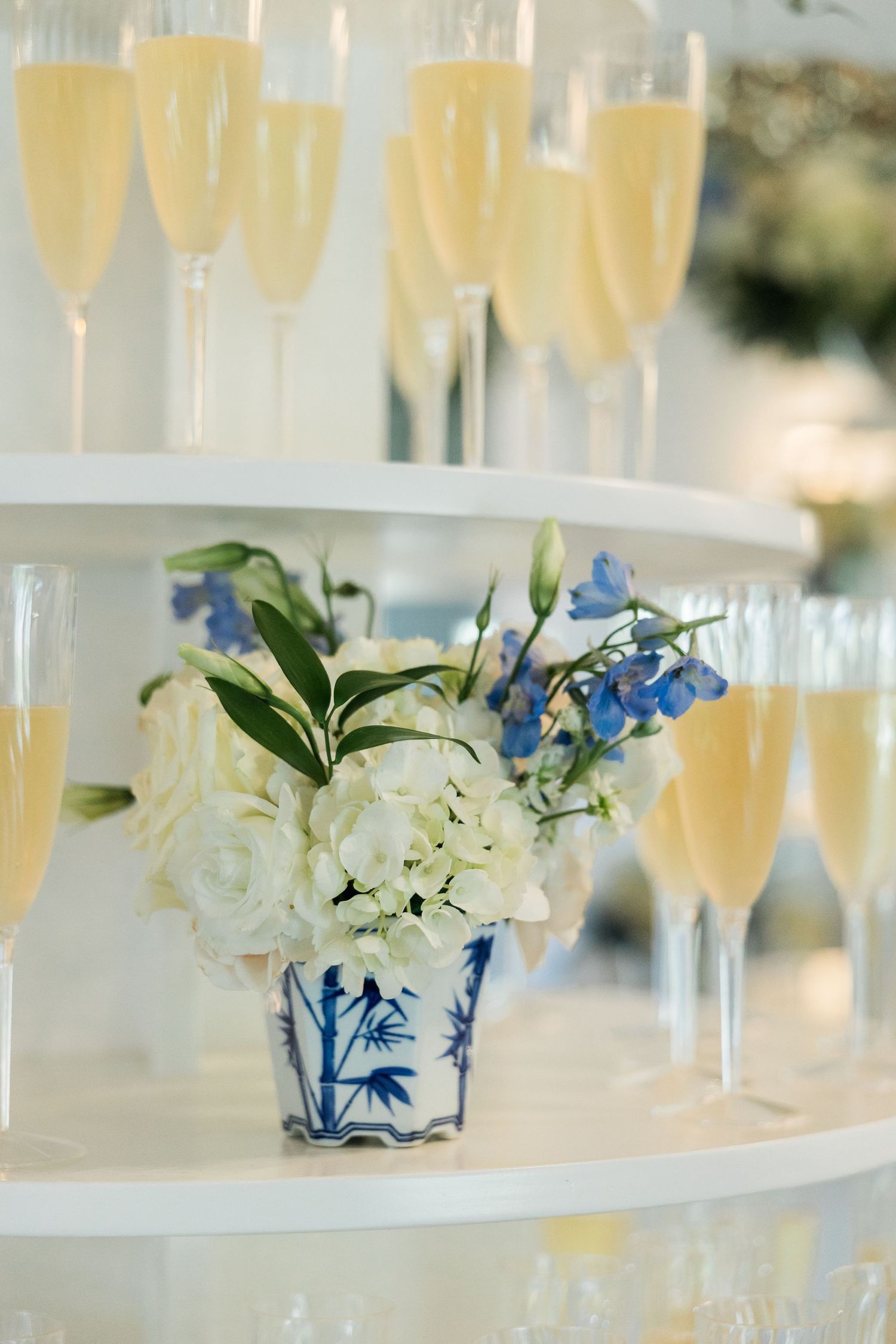 Elegant champagne tower display with white and blue floral arrangement at wedding reception.