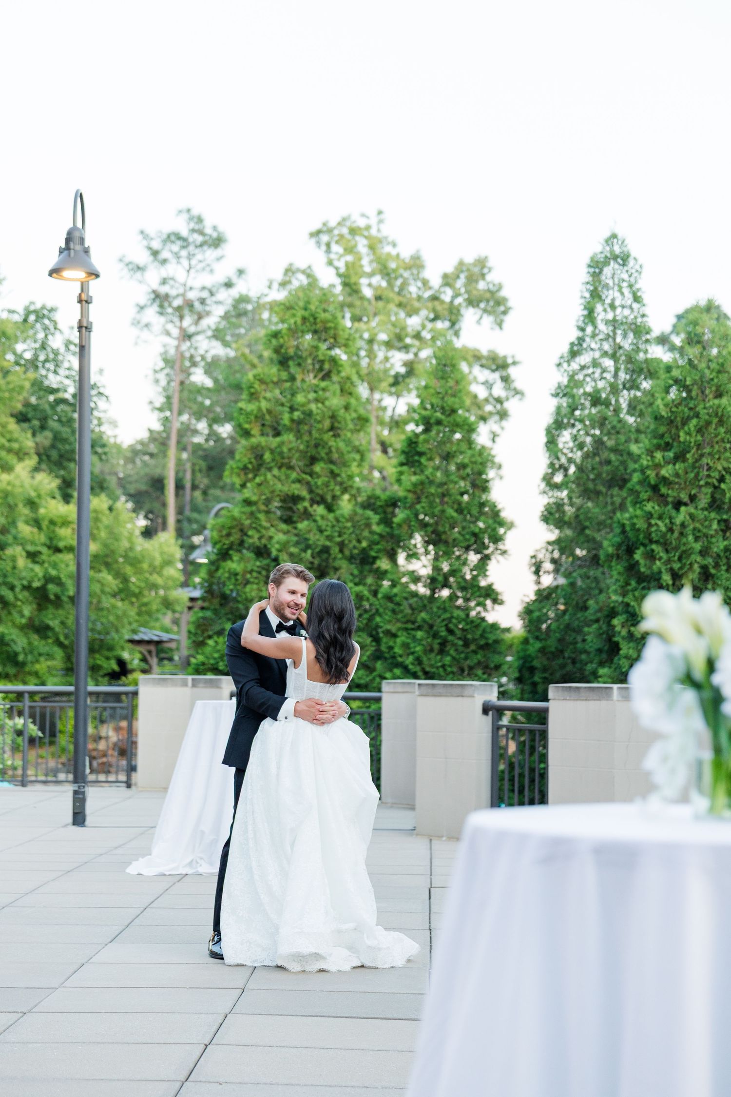 Bride and groom share first dance on outdoor terrace surrounded by lush green trees at elegant wedding reception.