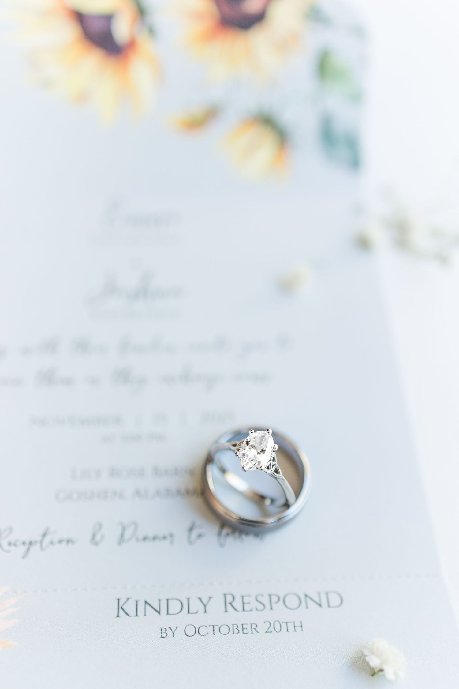 Wedding rings resting on a sunflower-themed RSVP card with a diamond engagement ring, due October 20th.
