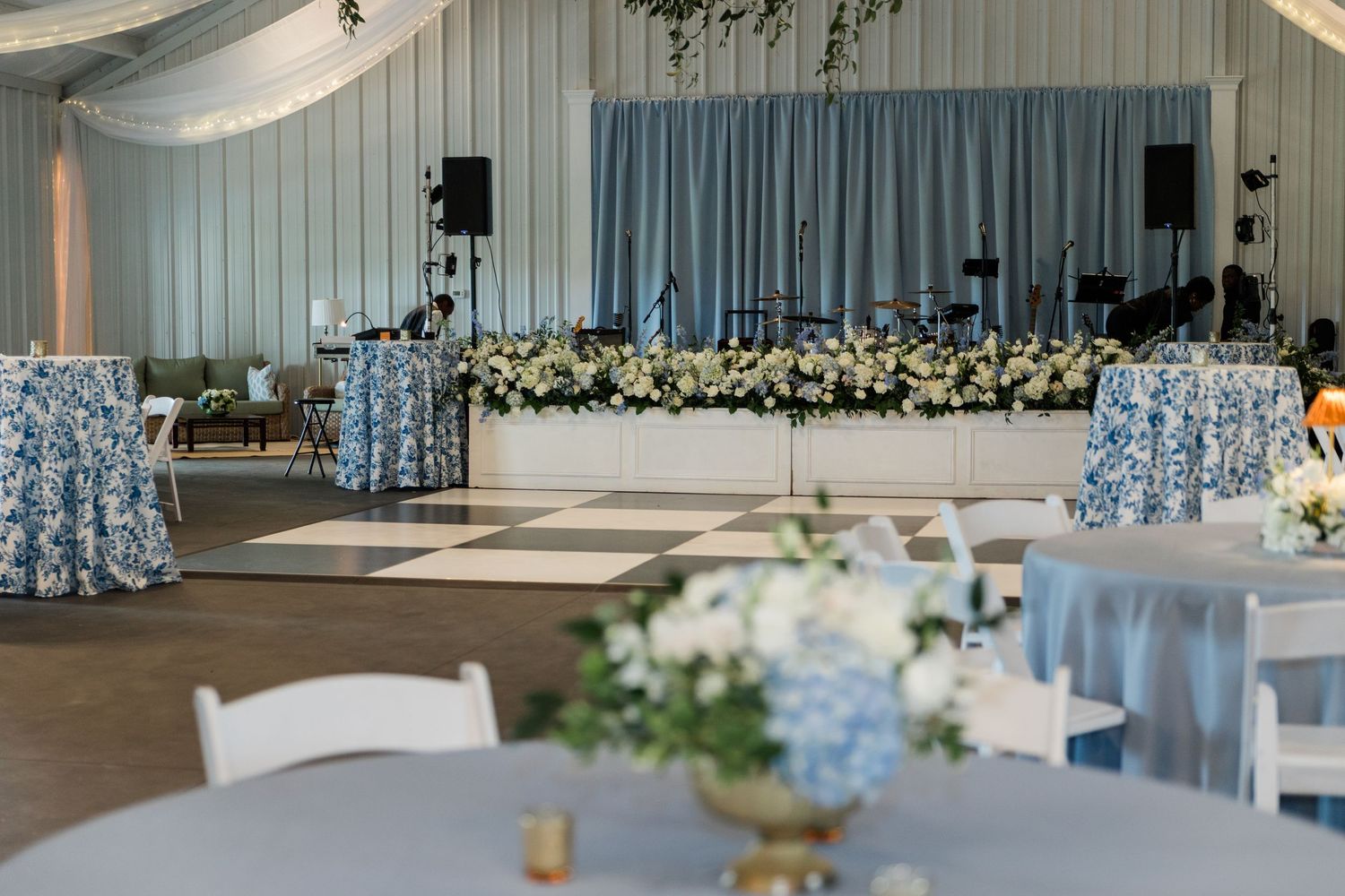Wedding reception venue with dance floor, stage, floral arrangements, and blue and white decor.