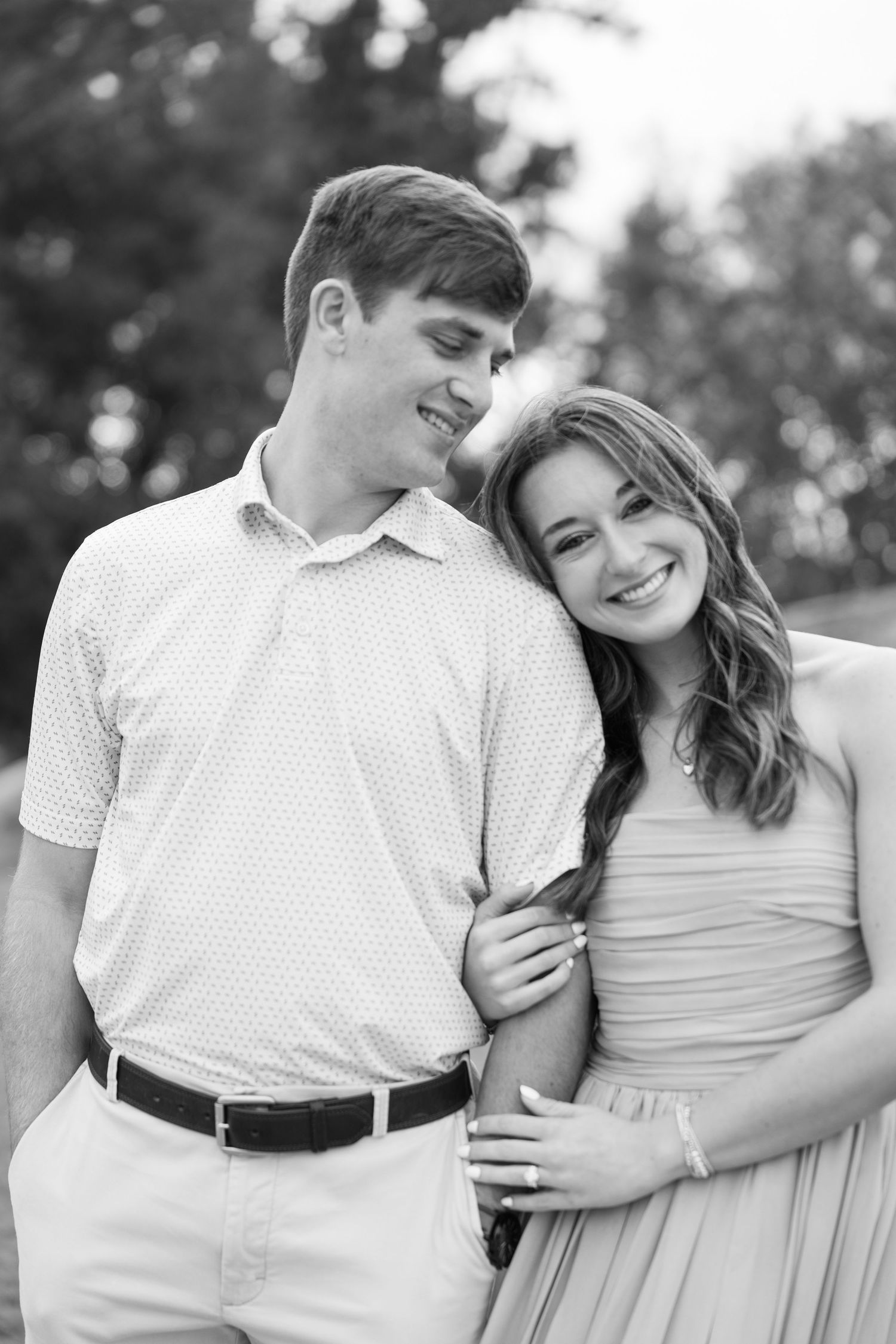 Black and white portrait of a smiling couple arm in arm, the man looking down at the woman as she leans against his shoulder.