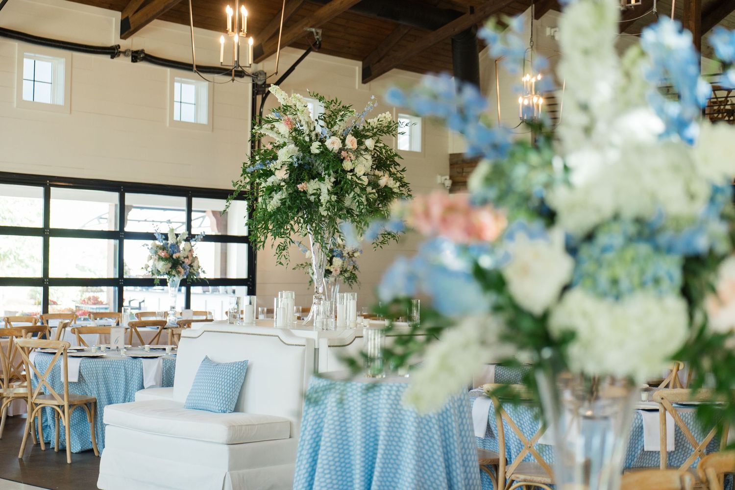 Elegant wedding reception hall with blue floral tablecloths, tall white flower centerpieces, and chandelier lighting.