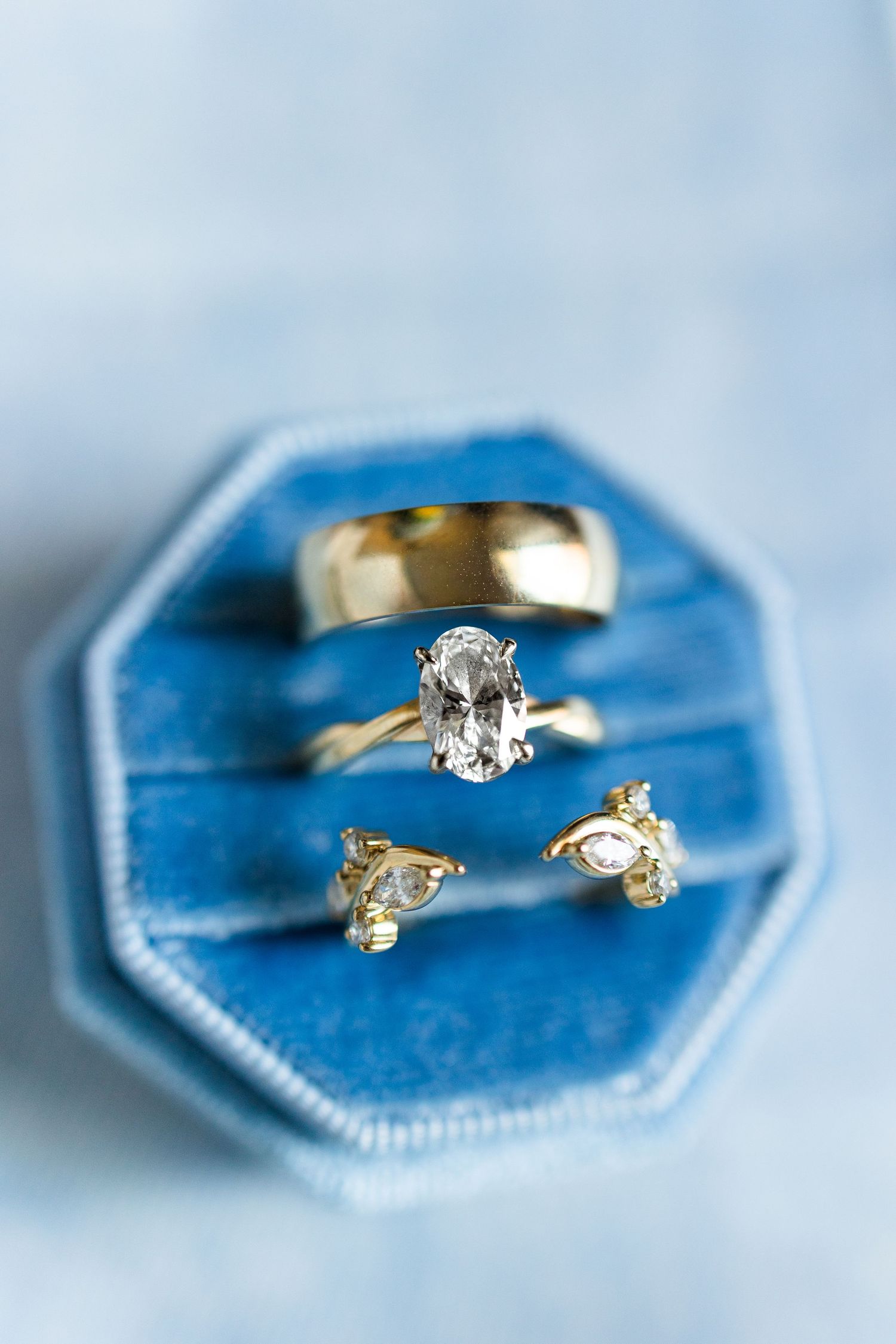 Three gold rings with diamonds displayed in a blue velvet octagonal ring box on a light blue background.