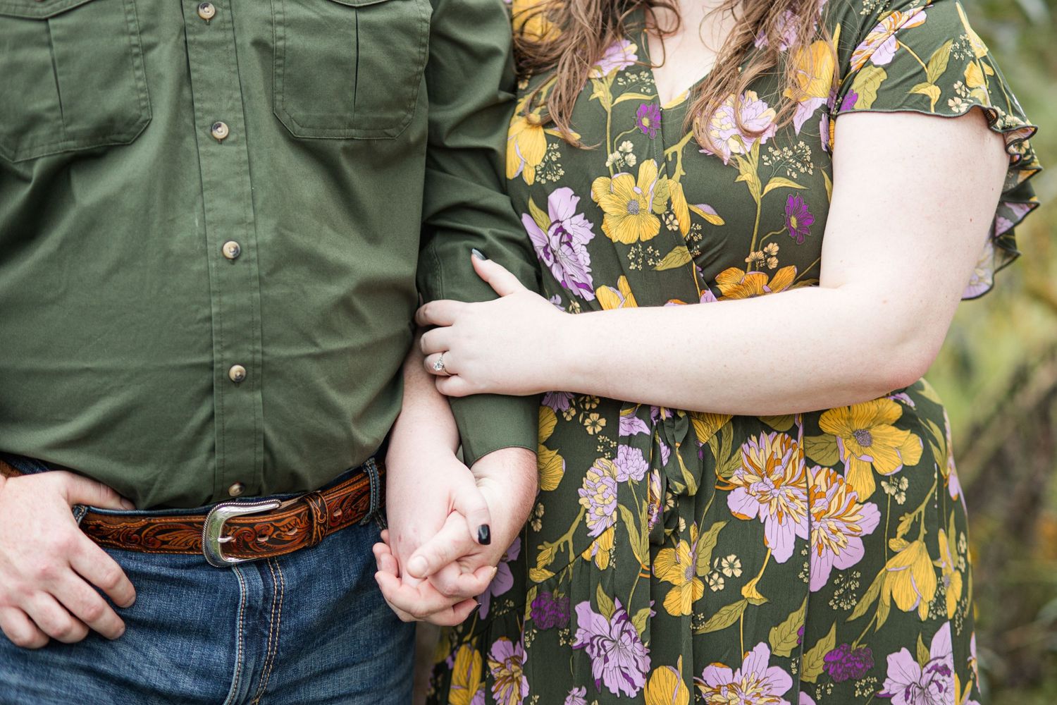 Couple holding hands outdoors, man in green shirt and woman in floral dress, romantic engagement photo.