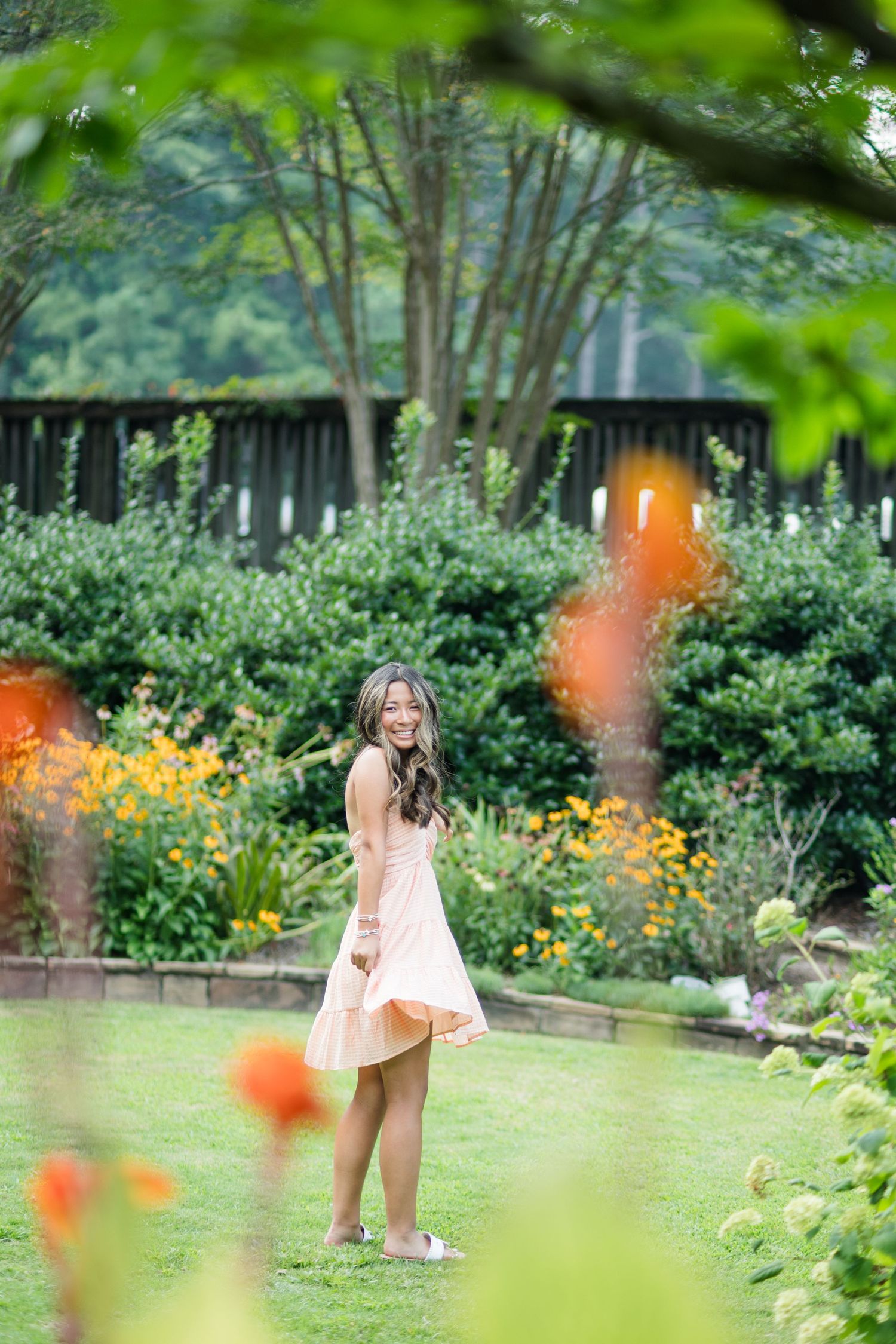 Young woman in peach dress spinning joyfully in vibrant garden with orange flowers.