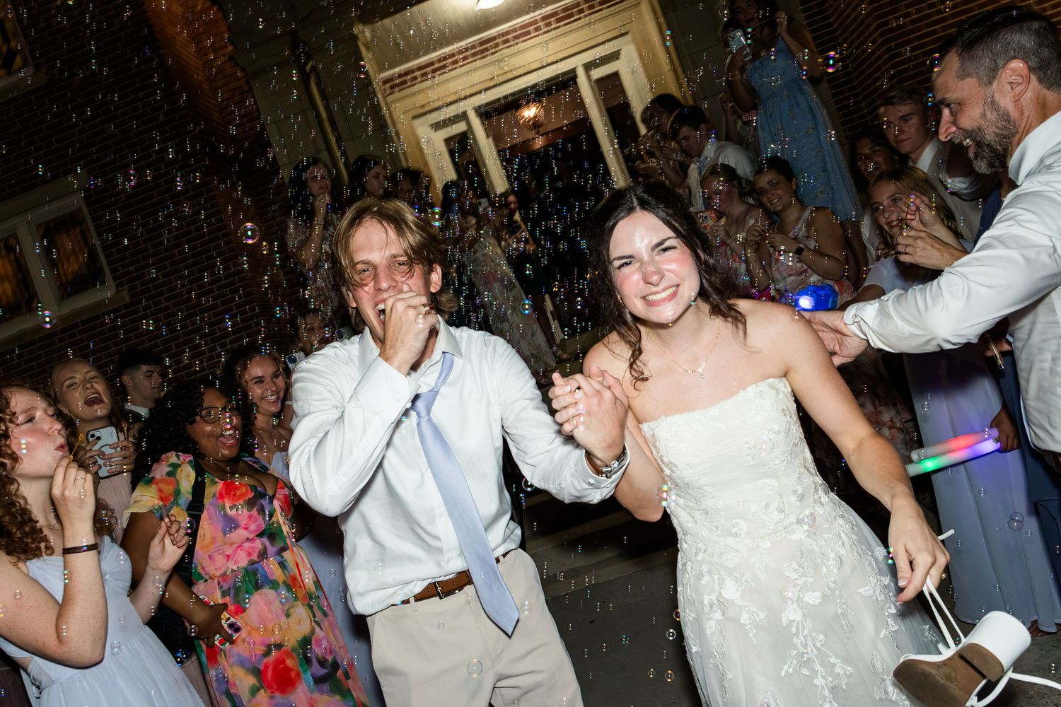 Bride in white gown and groom celebrate joyfully as confetti falls during lively wedding reception send-off.