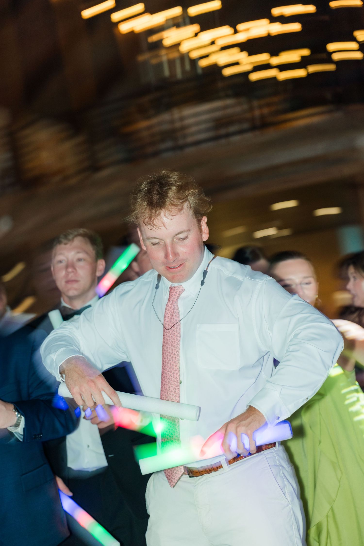 Wedding guest dances energetically with colorful glow sticks at lively reception celebration.
