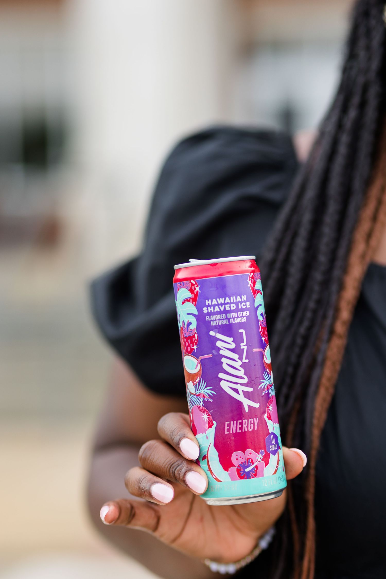 Woman holding a colorful Alani Nu Hawaiian Shaved Ice Energy drink can outdoors.