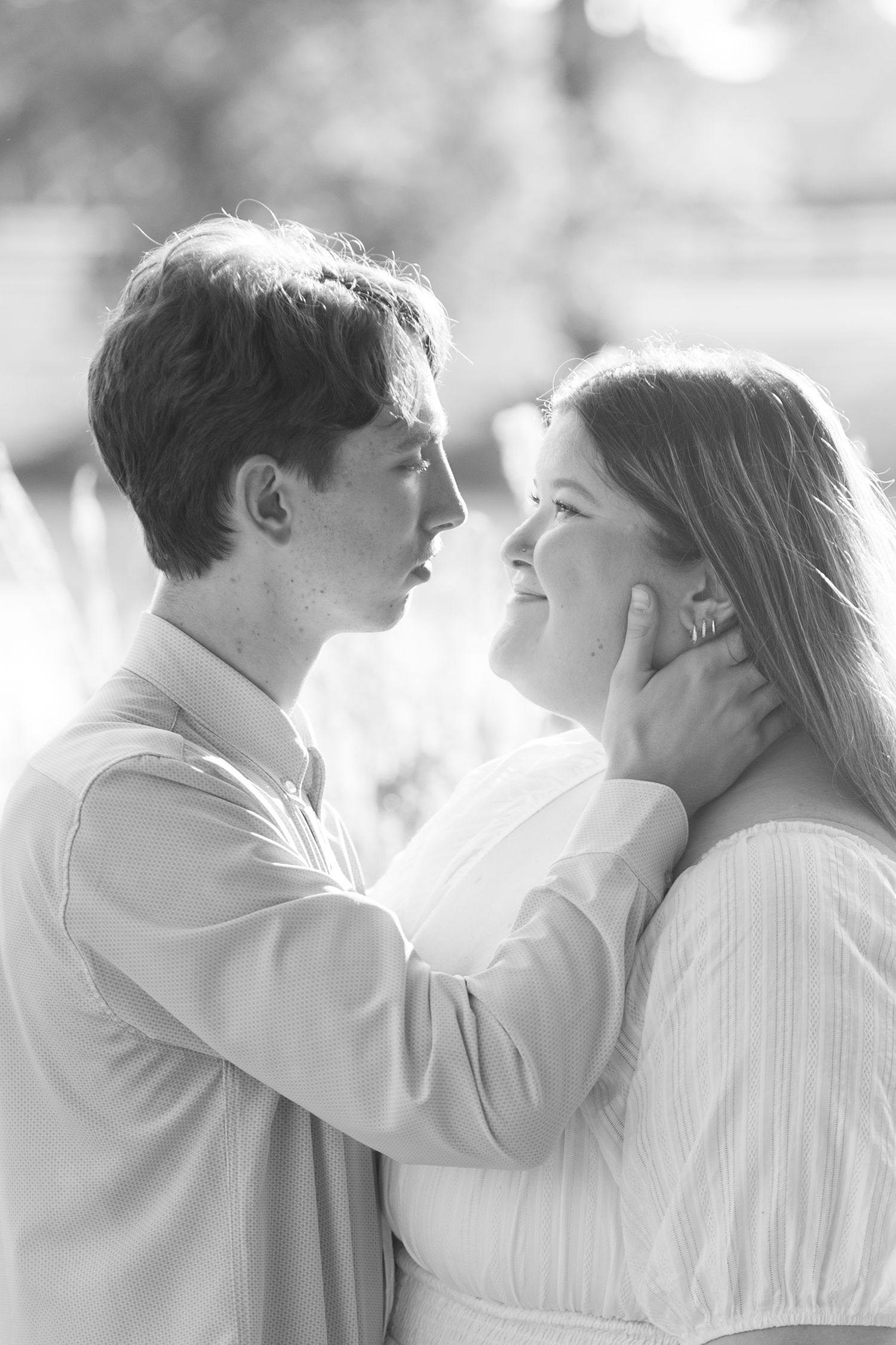 Black and white photo of a romantic couple gazing at each other, man gently cupping woman's face outdoors.