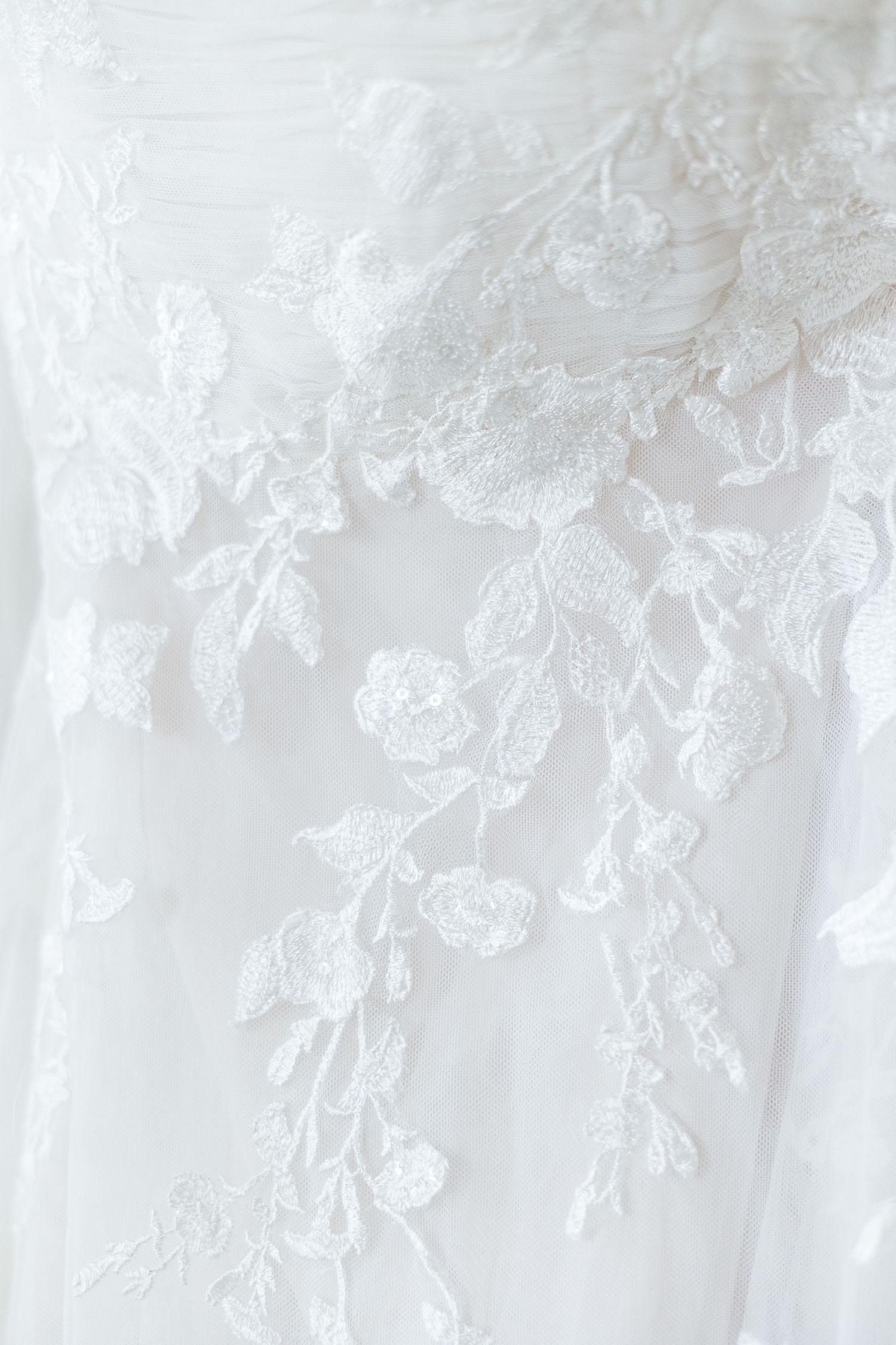 Close-up of intricate white floral lace embroidery on a bridal wedding gown.