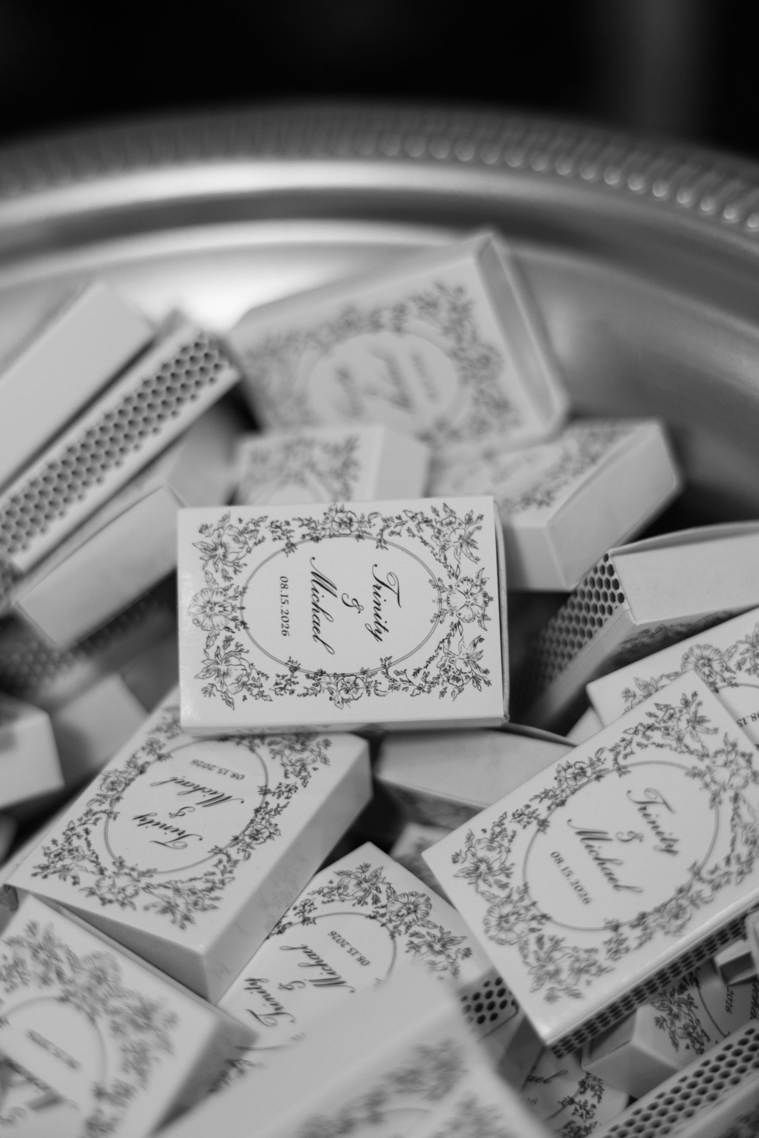 Black and white photo of personalized wedding matchbox favors with elegant script design on a silver tray.