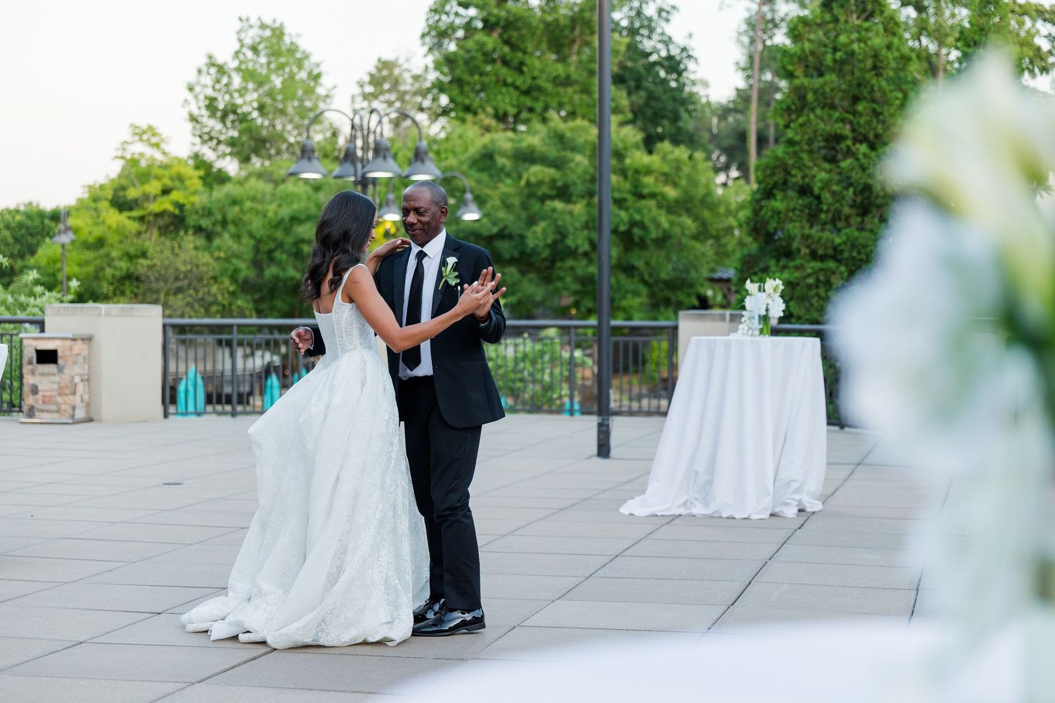 Bride and groom share their first dance on an outdoor patio at a wedding reception surrounded by elegant white floral decor.