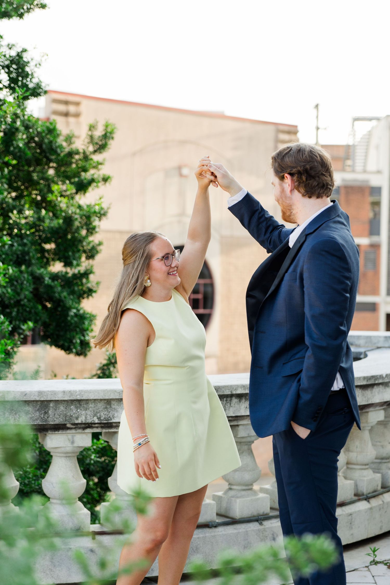Couple dancing outdoors on a terrace, woman in mint dress, man in navy suit, holding hands raised.