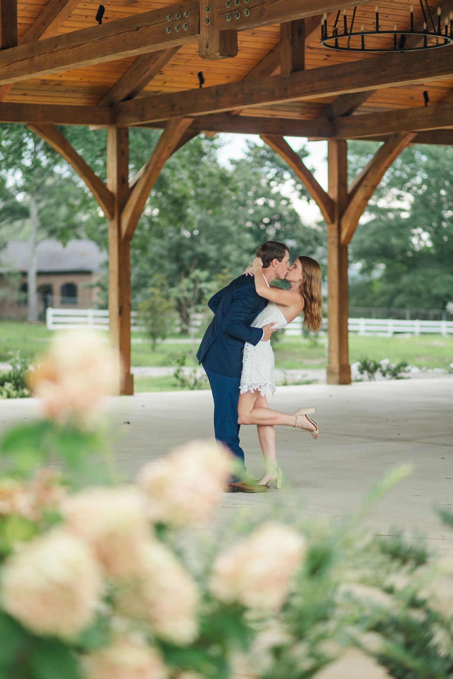 Couple sharing a romantic kiss under a wooden pavilion surrounded by blooming roses.