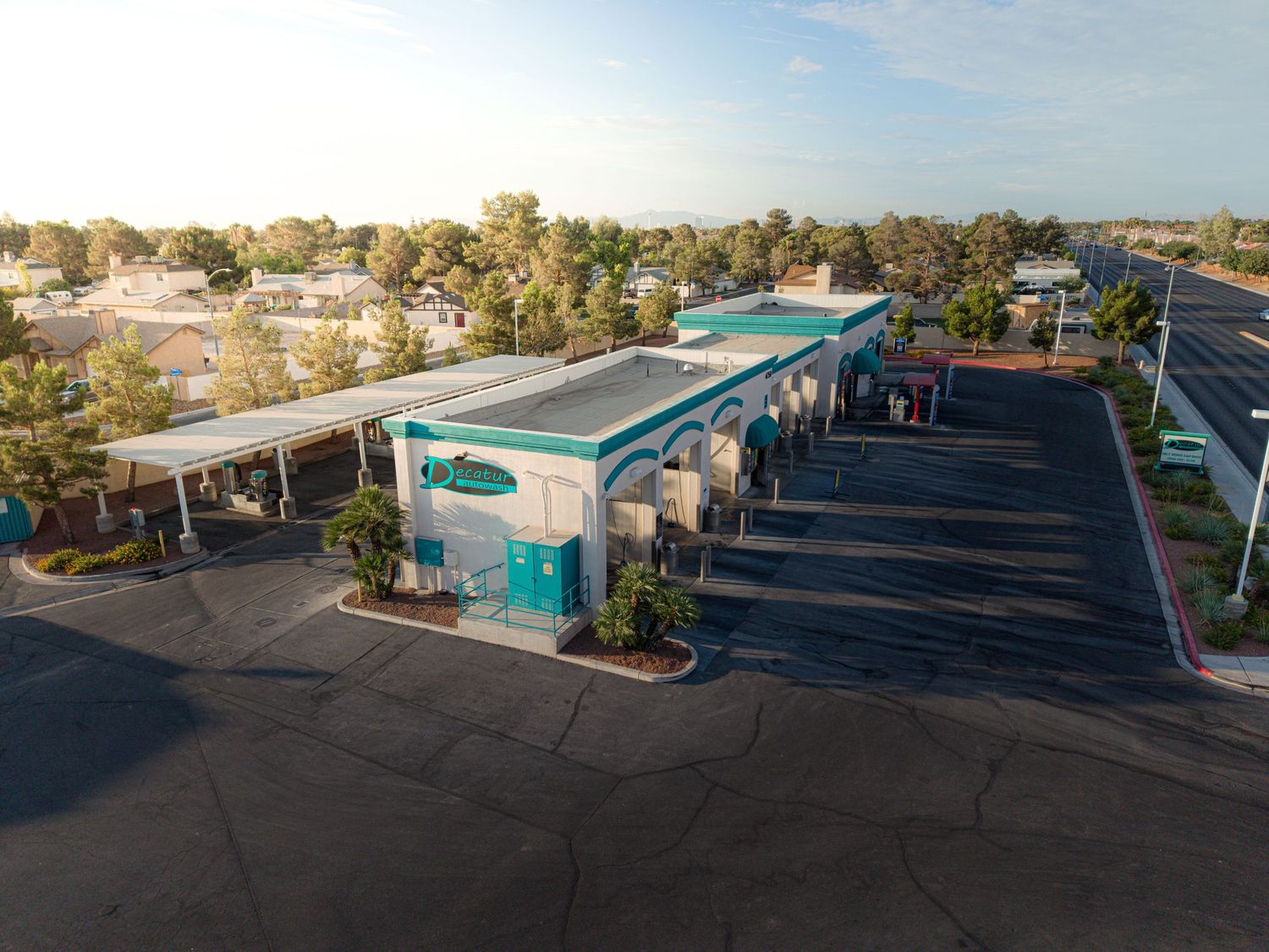 Aerial view of a teal and white car wash facility with covered bays and spacious parking lot at sunset.
