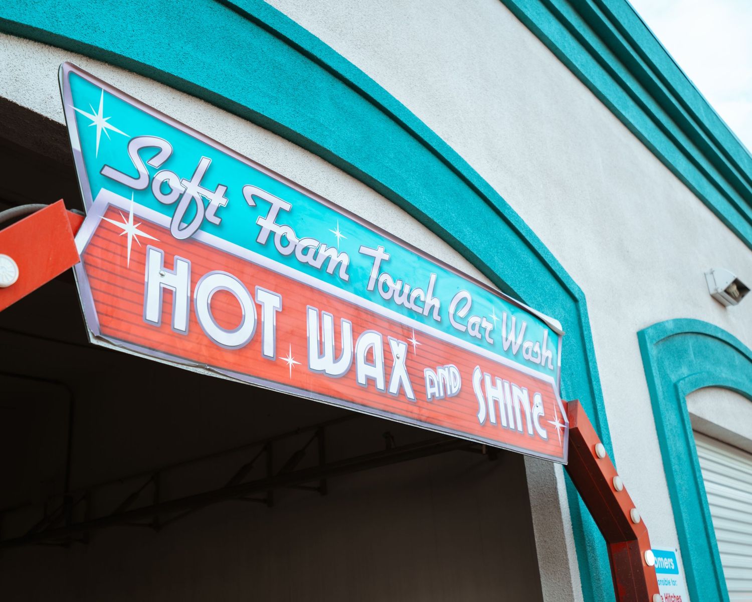 Retro teal and red sign for Soft Foam Touch Car Wash Hot Wax and Shine on a vintage-style building.