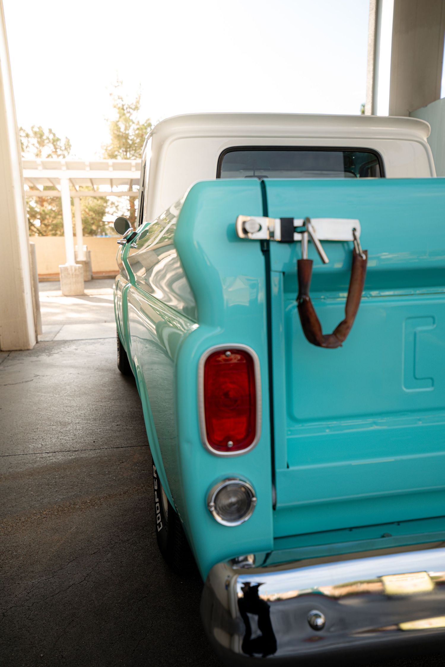 Vintage turquoise pickup truck parked in garage, showcasing classic tail lights and chrome bumper details.